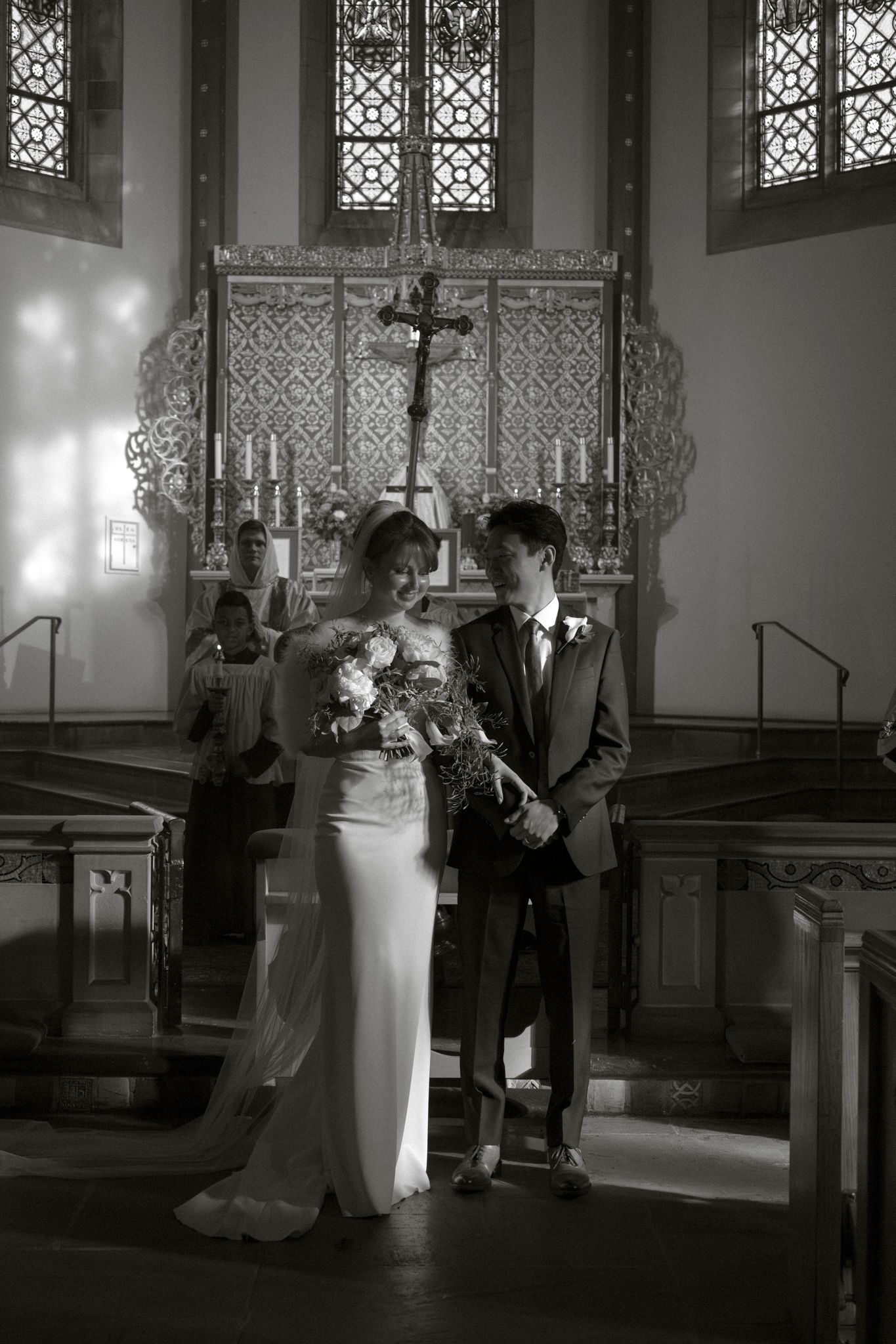 Bride and groom stand together at a church altar in a classic black and white wedding photo.