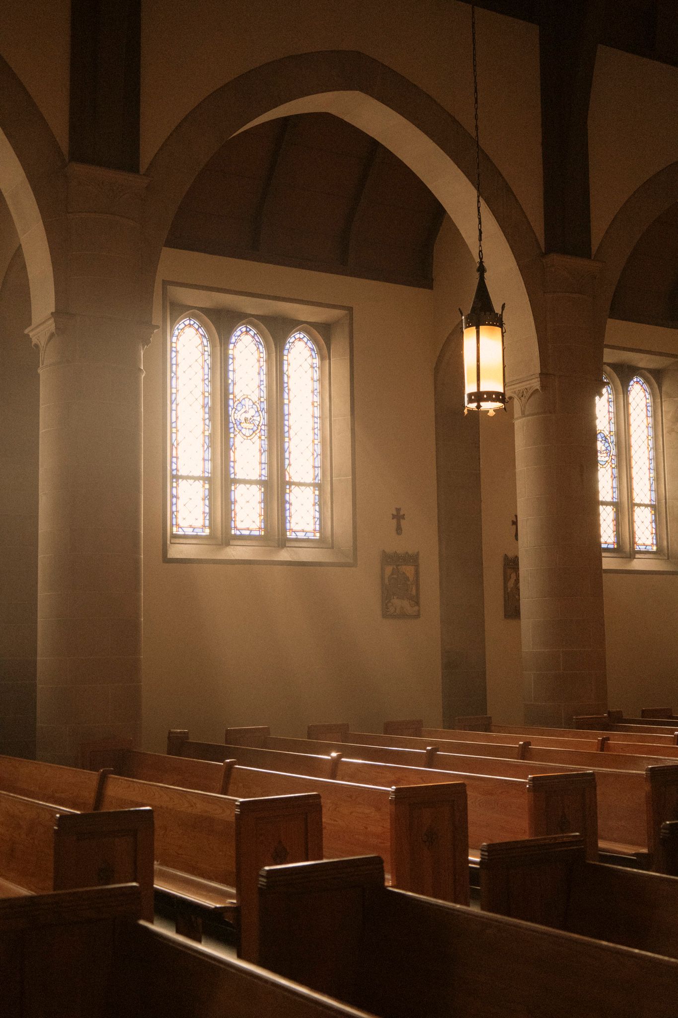 Sunlight streams through stained glass windows illuminating empty wooden pews in a historic stone church.