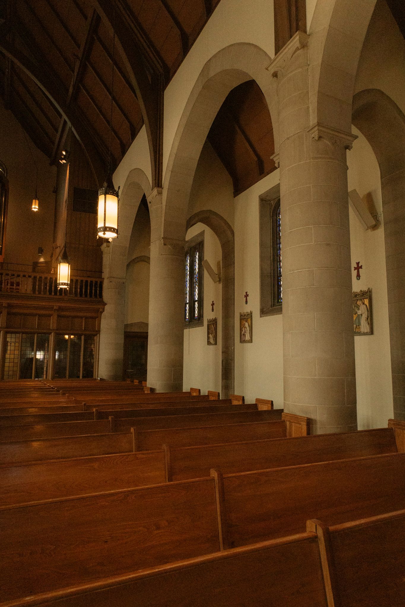 Interior of a church with wooden pews, stone arches, and warm pendant lighting in a traditional nave.