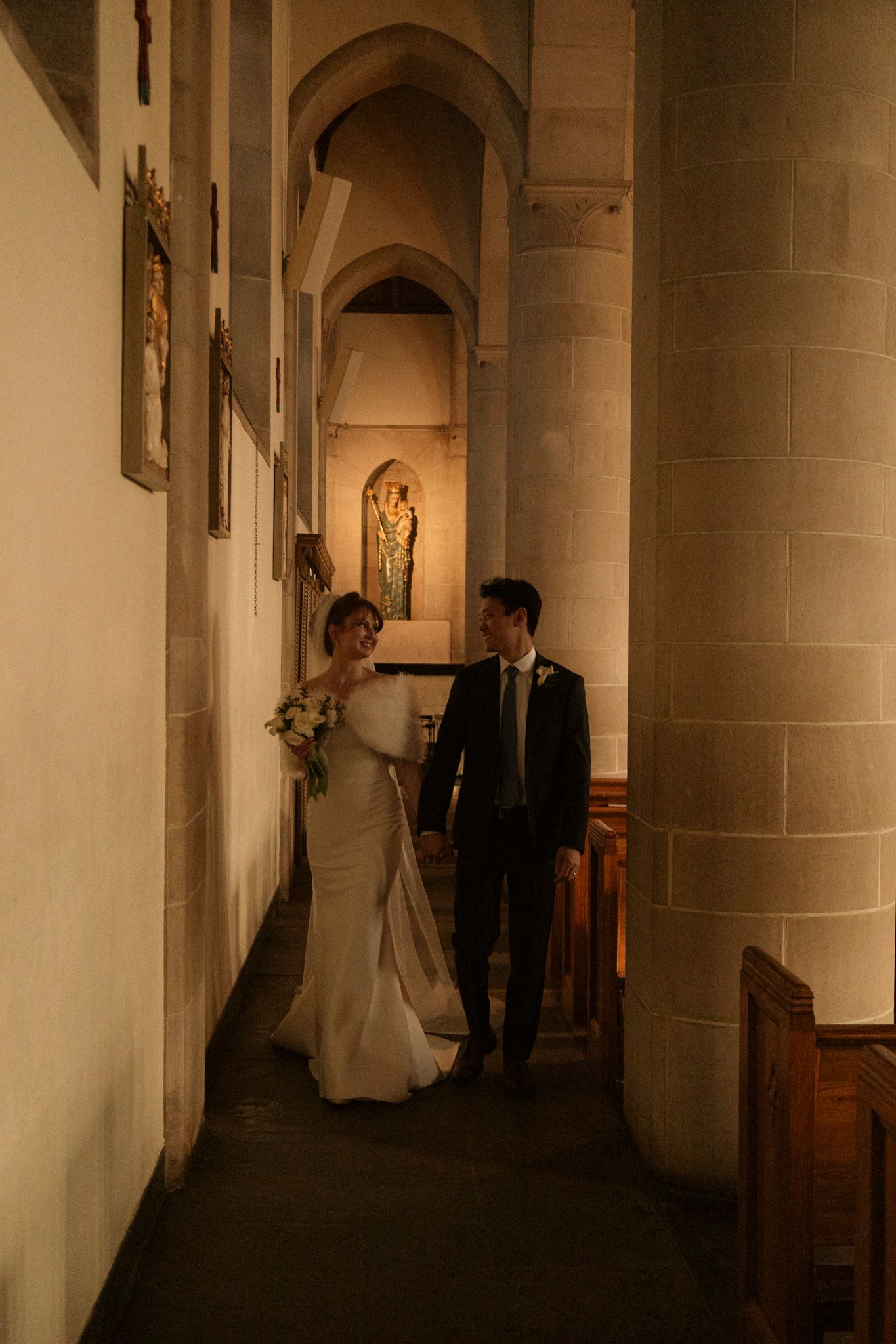 Bride and groom walking through a warmly lit stone church aisle, bride holding a bouquet.