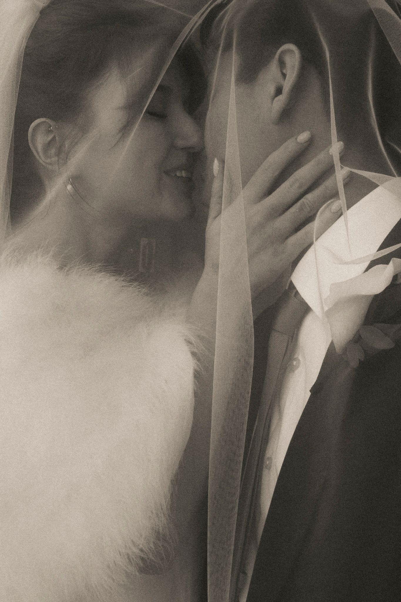 Romantic sepia-toned photo of bride and groom sharing an intimate moment under a flowing veil.