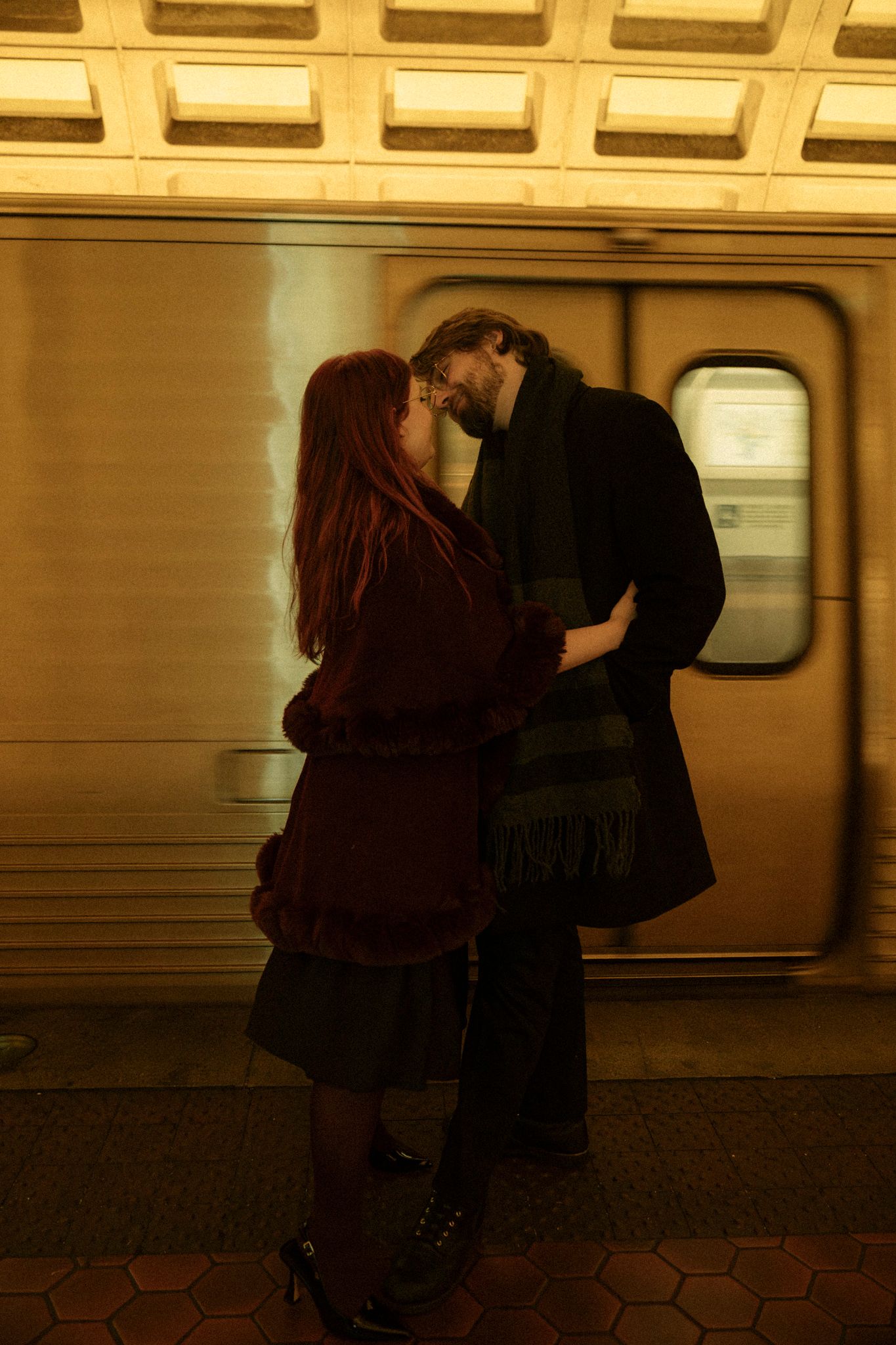 Two silhouettes embrace on a subway platform with a train car and tiled wall in the background.