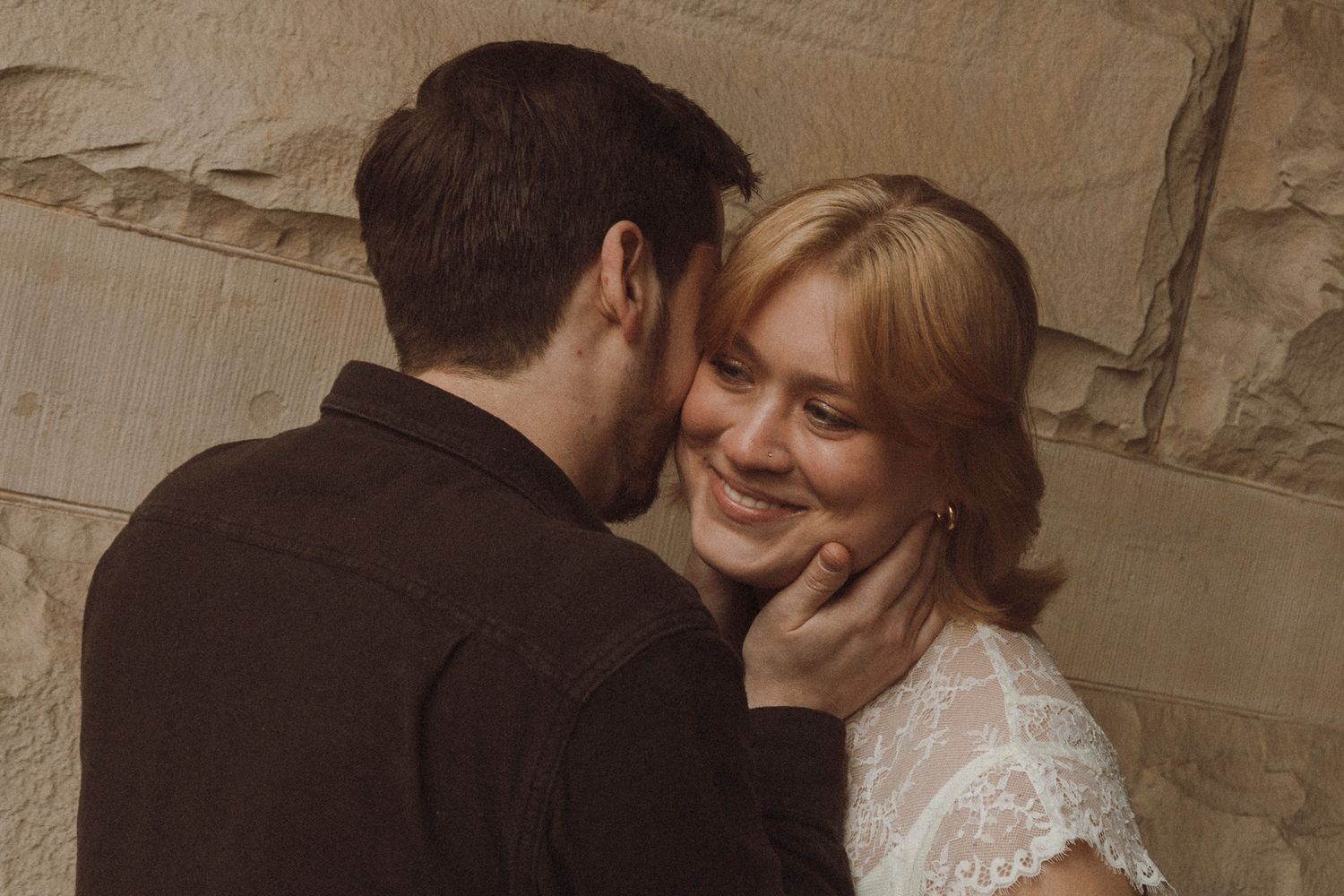 Bride and groom share an intimate moment against a stone wall background during their wedding celebration.