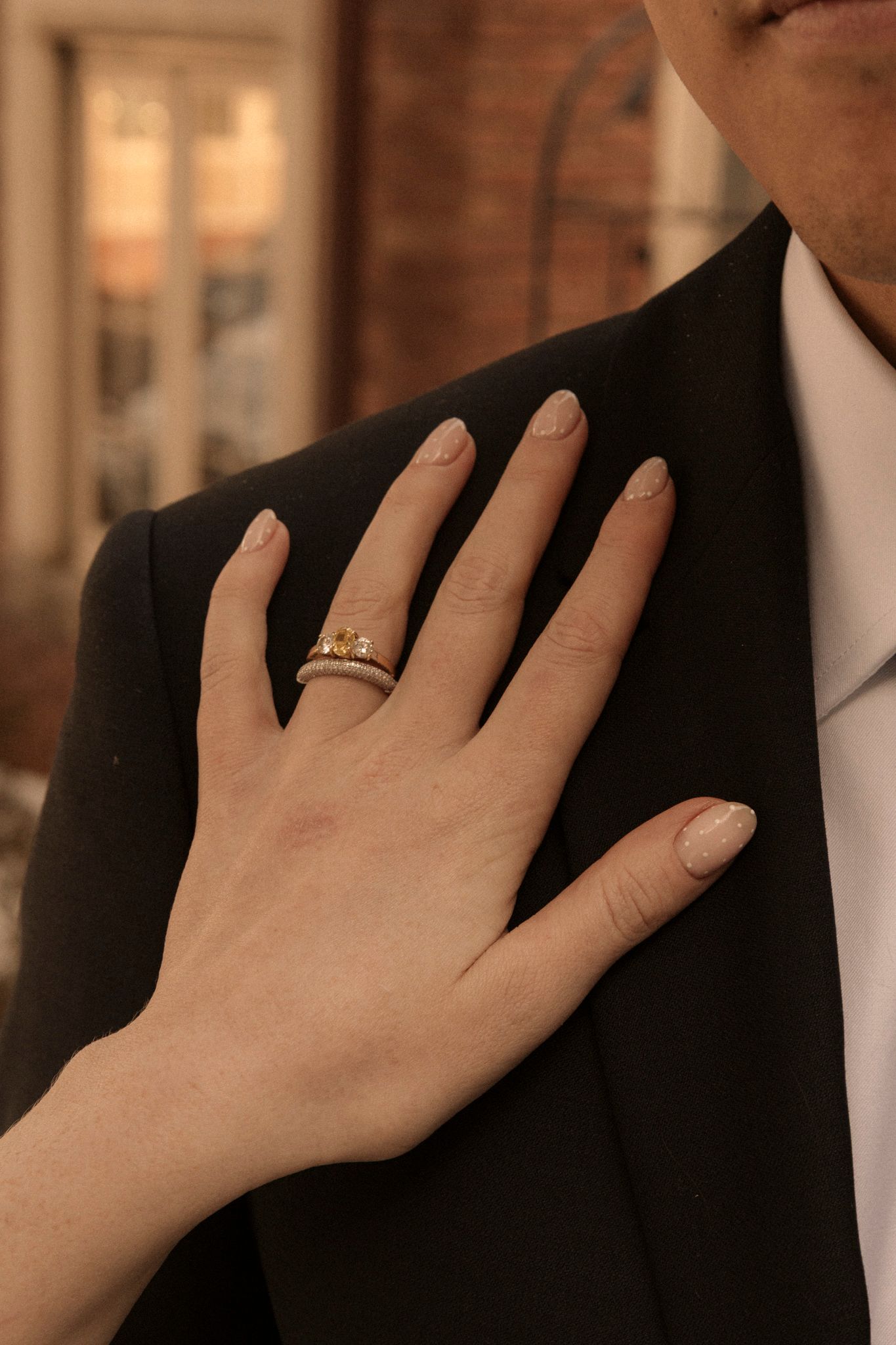 Close-up of bride's hand with gold wedding rings resting on groom's black suit jacket.