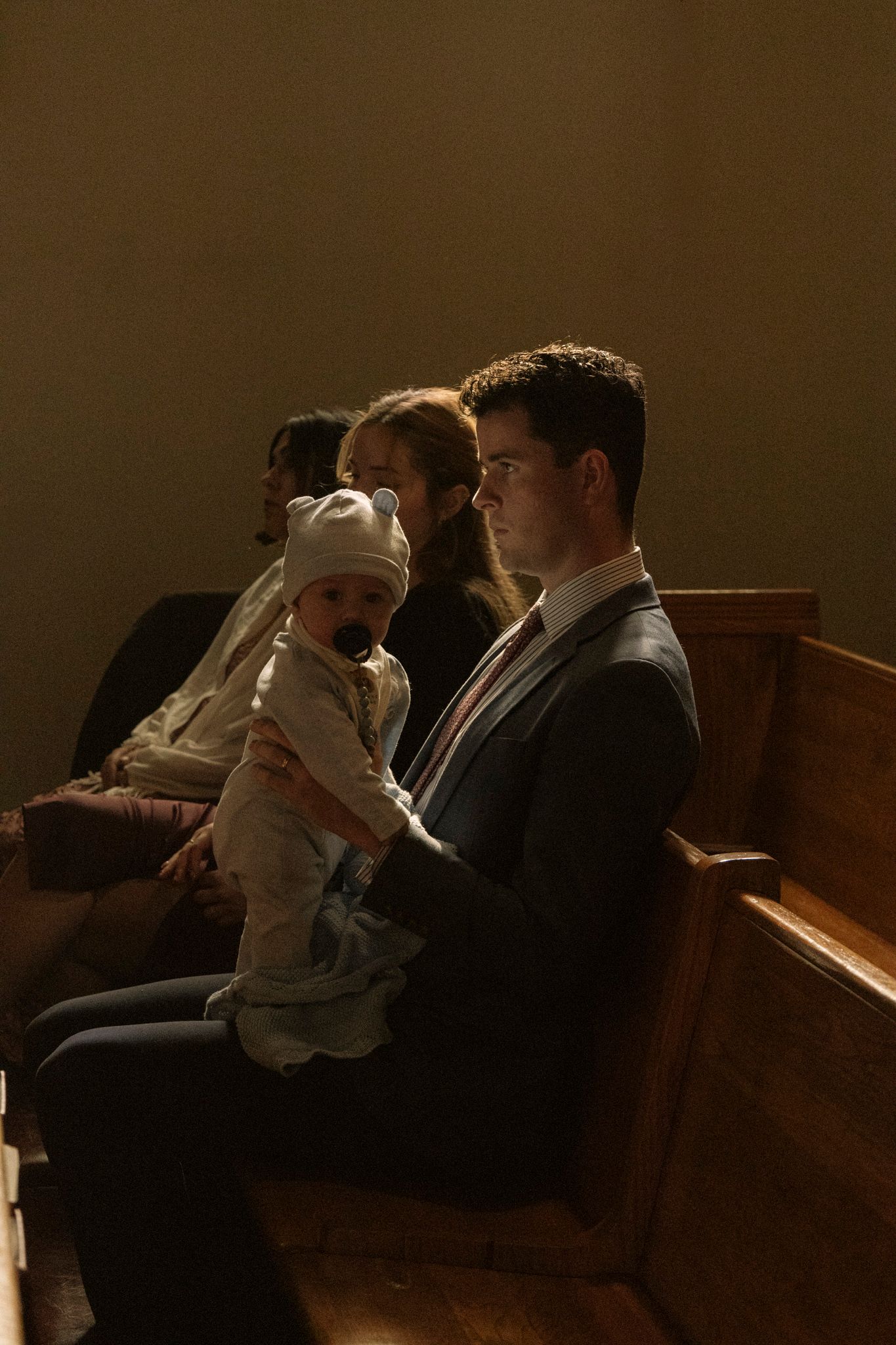 Man in suit holding baby in church pew during wedding ceremony.