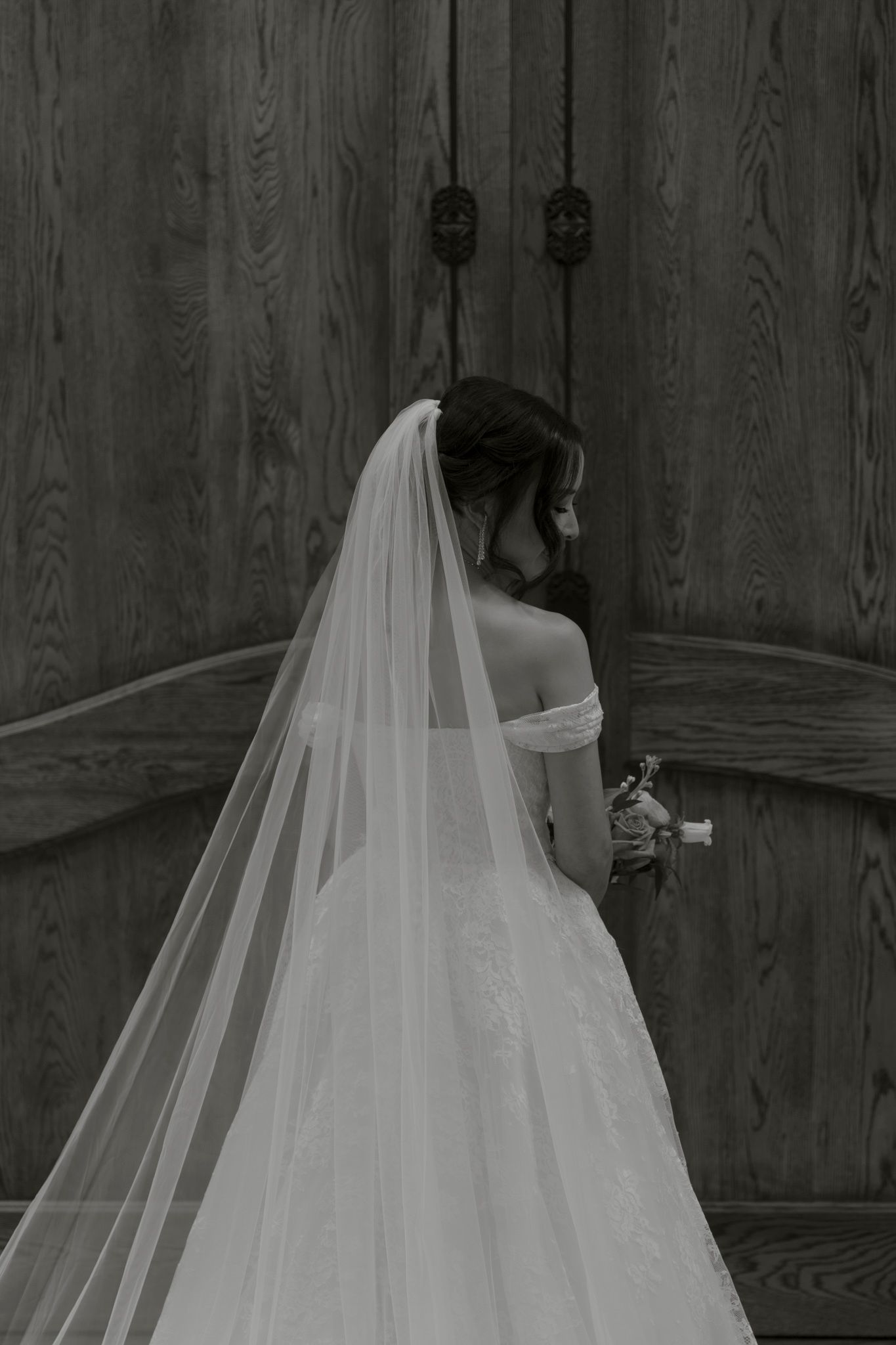 A dramatic black and white photo showing a flowing white wedding veil against a rustic wooden wall background.