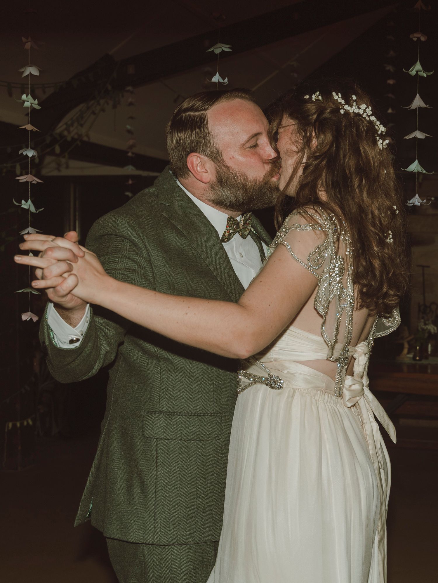 A couple shares a romantic dance at their wedding, with the bride in white and groom in a green suit.