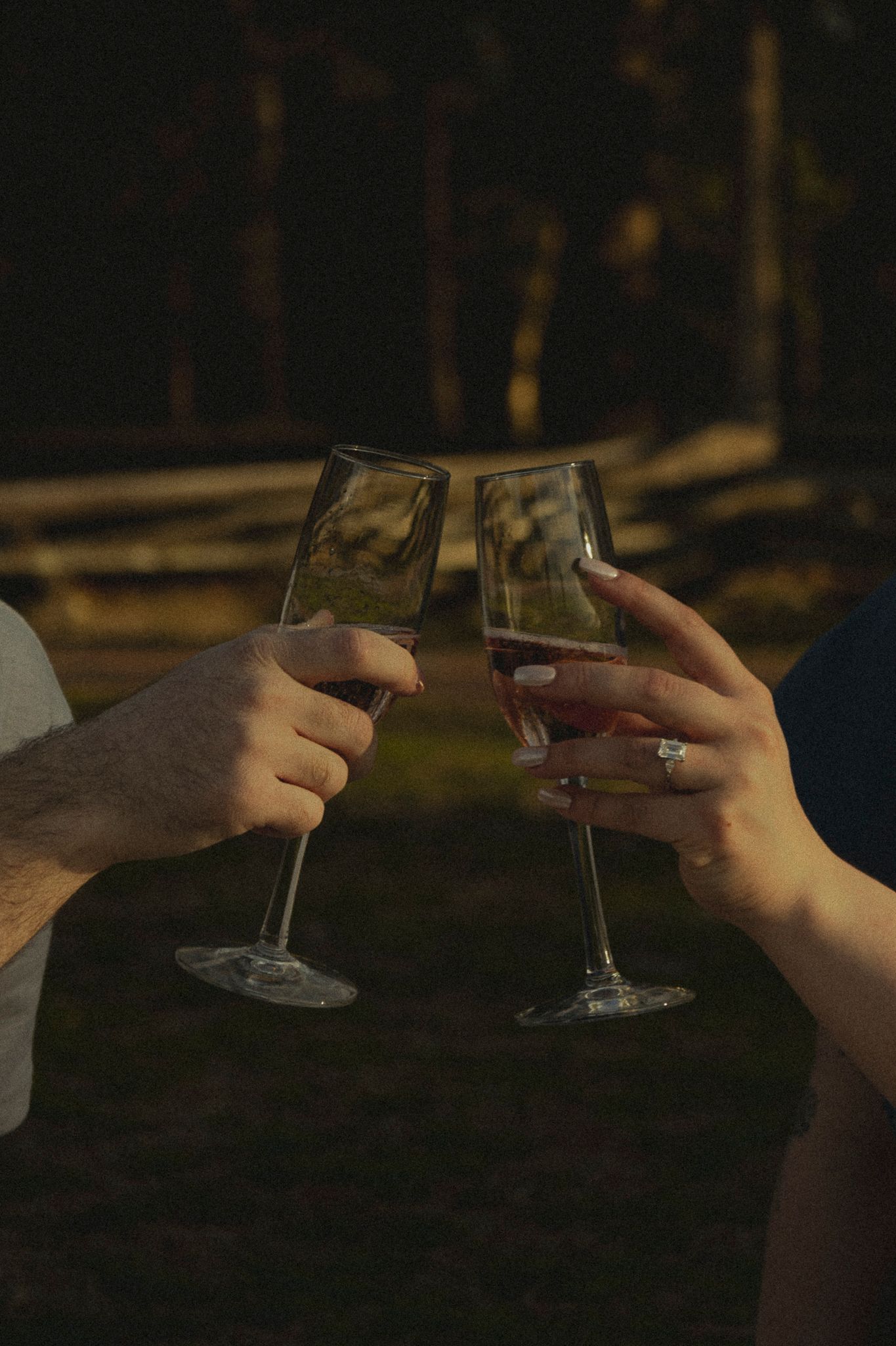 Close-up of couple clinking champagne glasses outdoors, woman wearing an engagement ring, celebrating together.