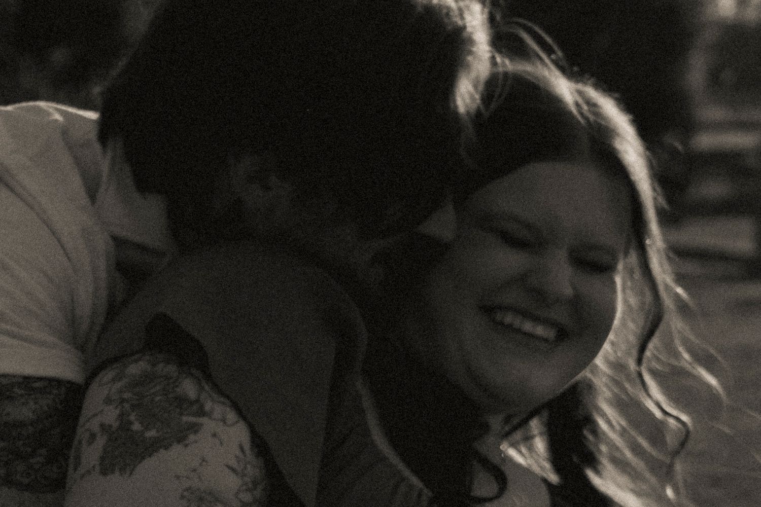 Black and white photo of a couple sharing a joyful embrace, woman smiling warmly as man hugs her closely.