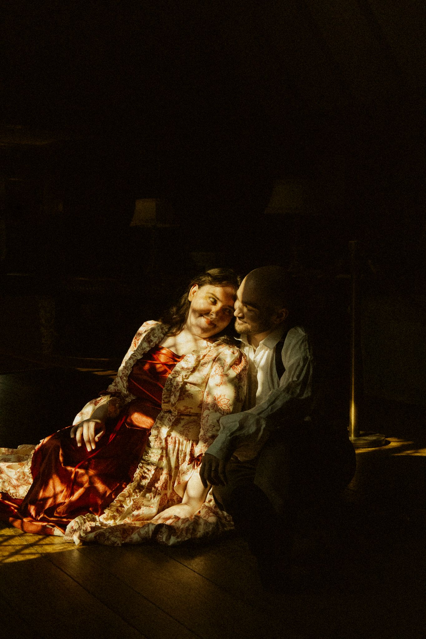 Romantic couple sitting together on floor in dramatic moody dark room with warm light.