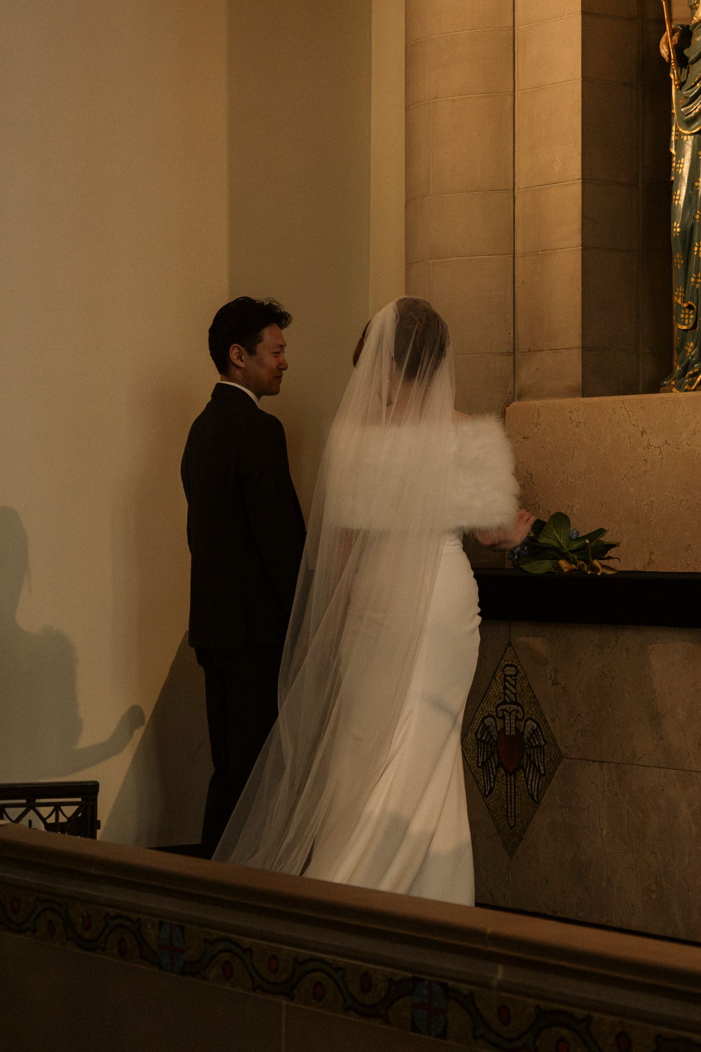 Bride in white gown and fur stole stands with groom at church altar during wedding ceremony.