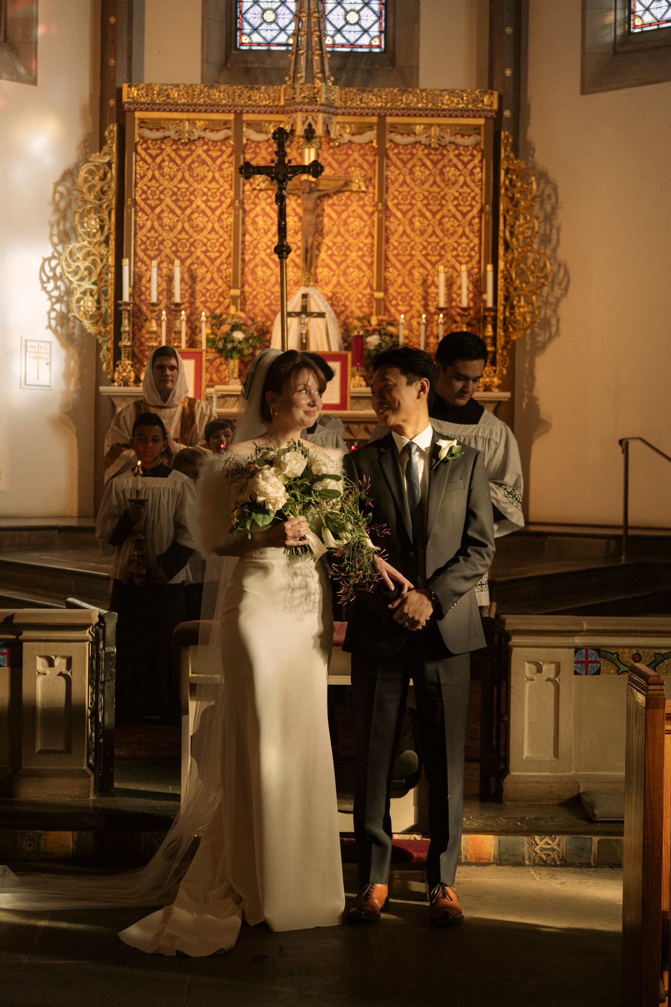 Bride and groom stand before golden altar in church after exchanging wedding vows.
