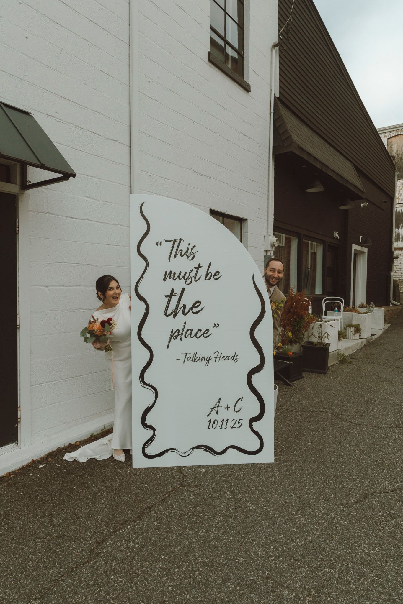 A couple poses against a white wall with artistic black swirls and text reading 'This must be the place'.
