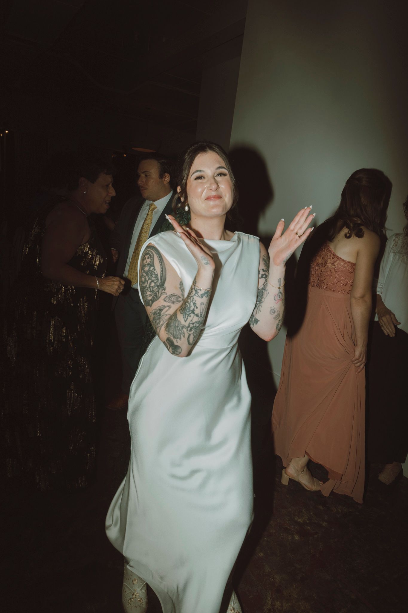 A guest in a white dress with tattoos dances at a wedding reception.