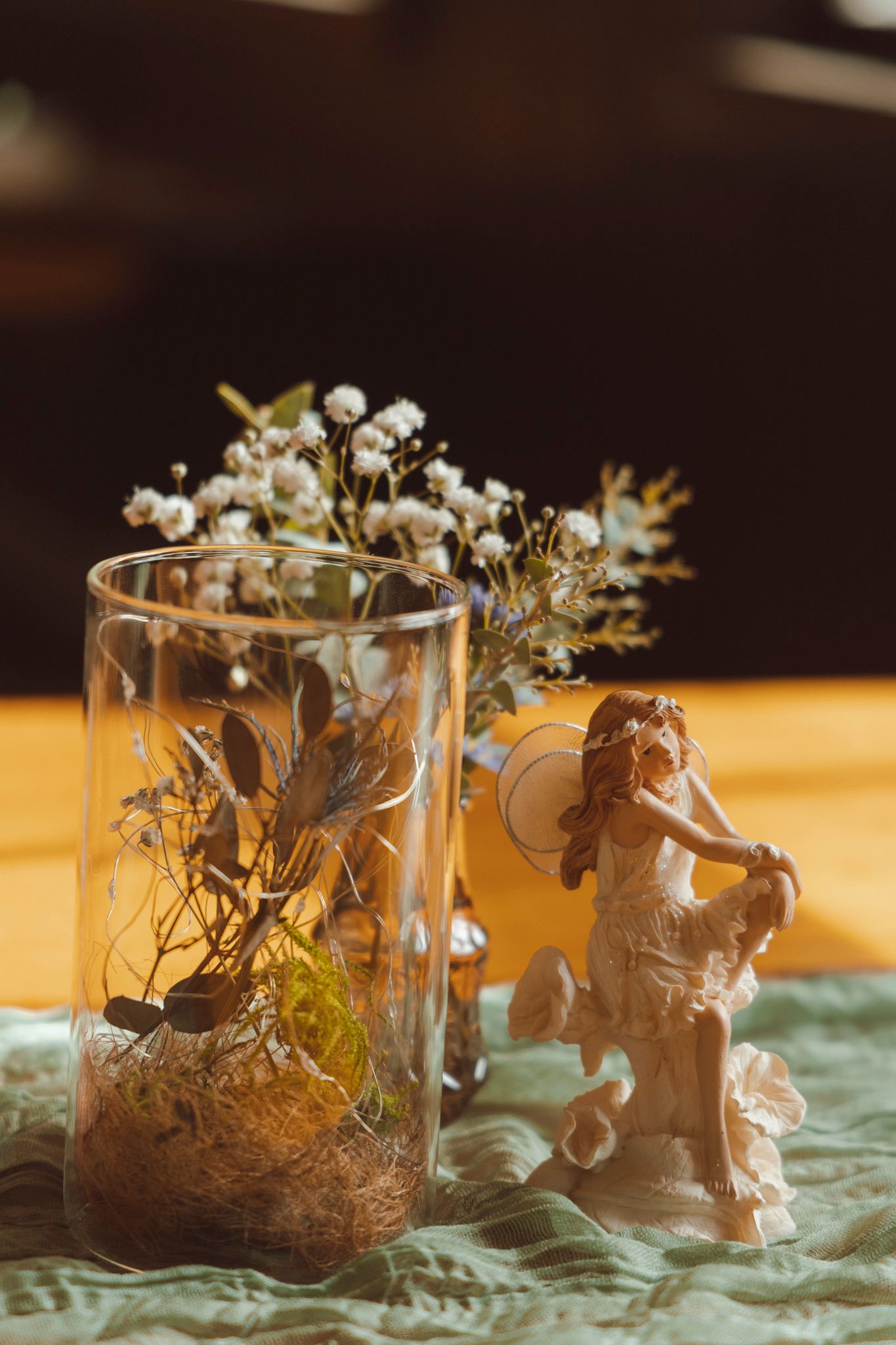 Small decorative glass terrariums with delicate baby's breath flowers and miniature fairy figurines create a whimsical display.