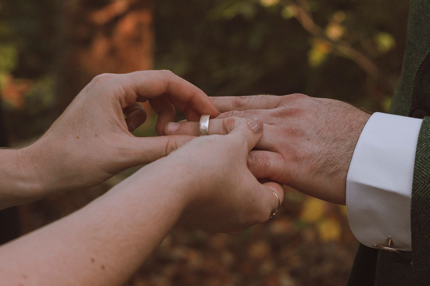 Close up view of hands exchanging wedding rings during a romantic outdoor ceremony.