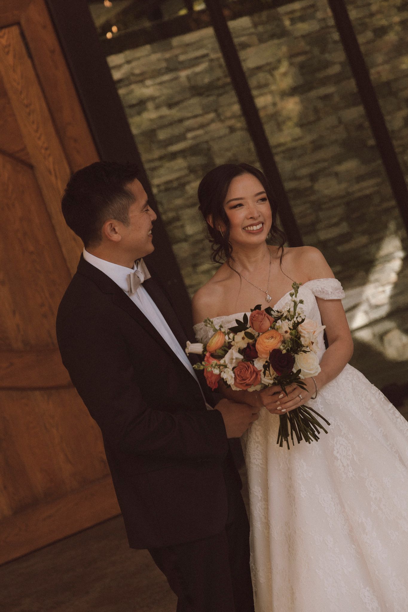 A tender wedding scene showing a couple sharing an intimate moment while holding a bouquet of peach and white flowers.