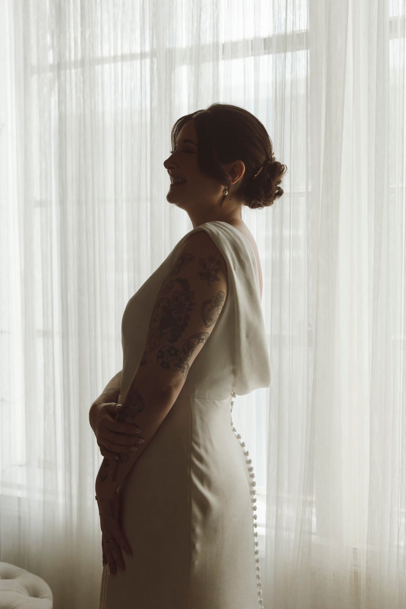 Silhouetted figure in a white dress stands by window with sheer curtains creating a dreamy atmosphere.