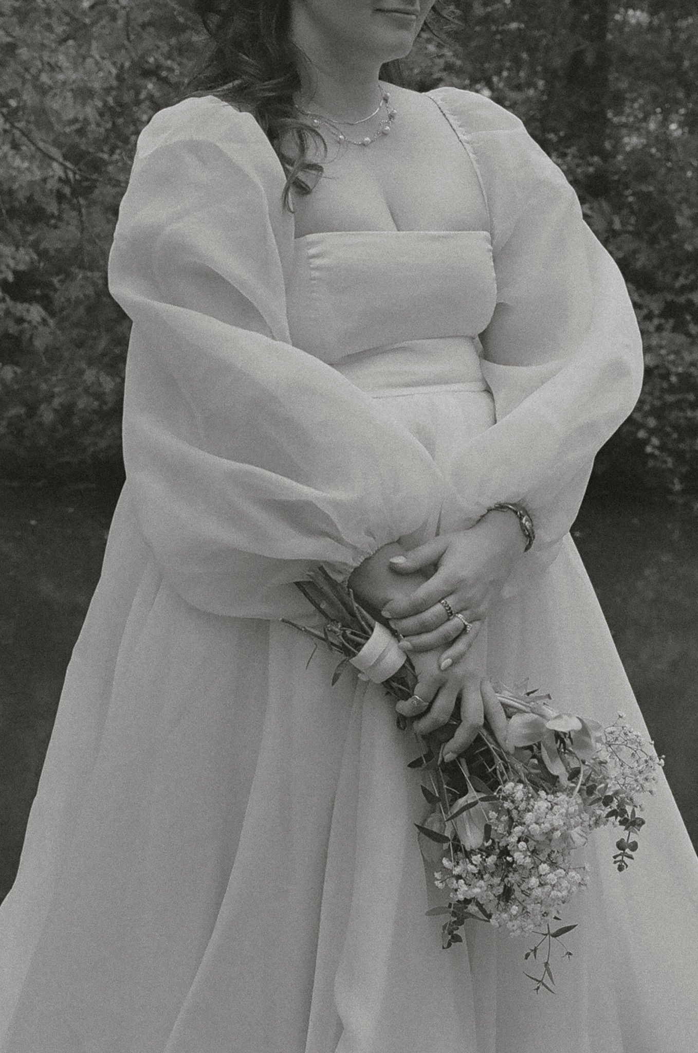 A series of black and white wedding photos showing close-up details of a bride in a white dress holding a small bouquet.