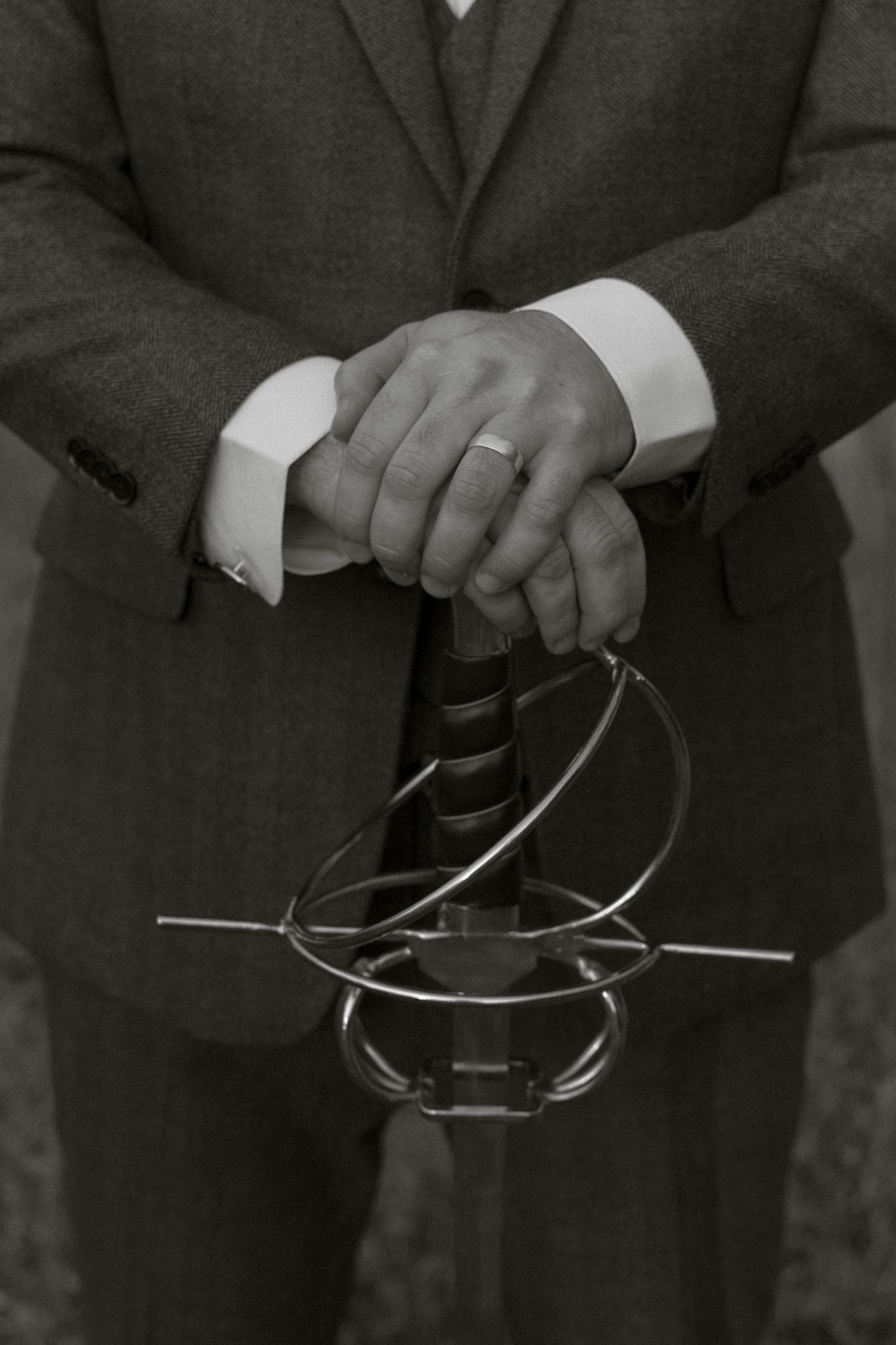 Black and white close-up of hands in formal attire holding a twisted metal wire sculpture or art piece.