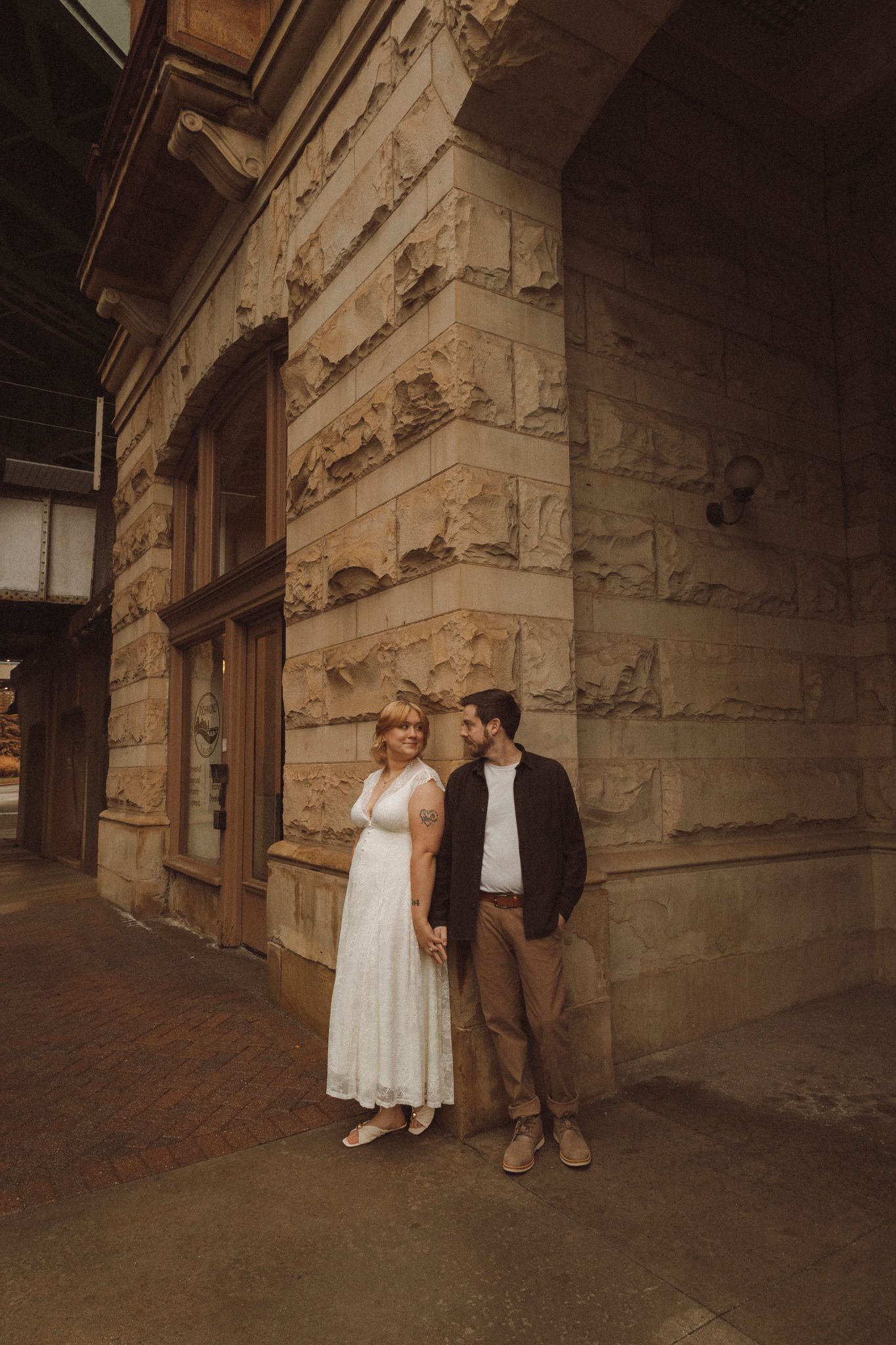 Couple stands in a rustic stone hallway with dramatic shadows and vintage aesthetic.
