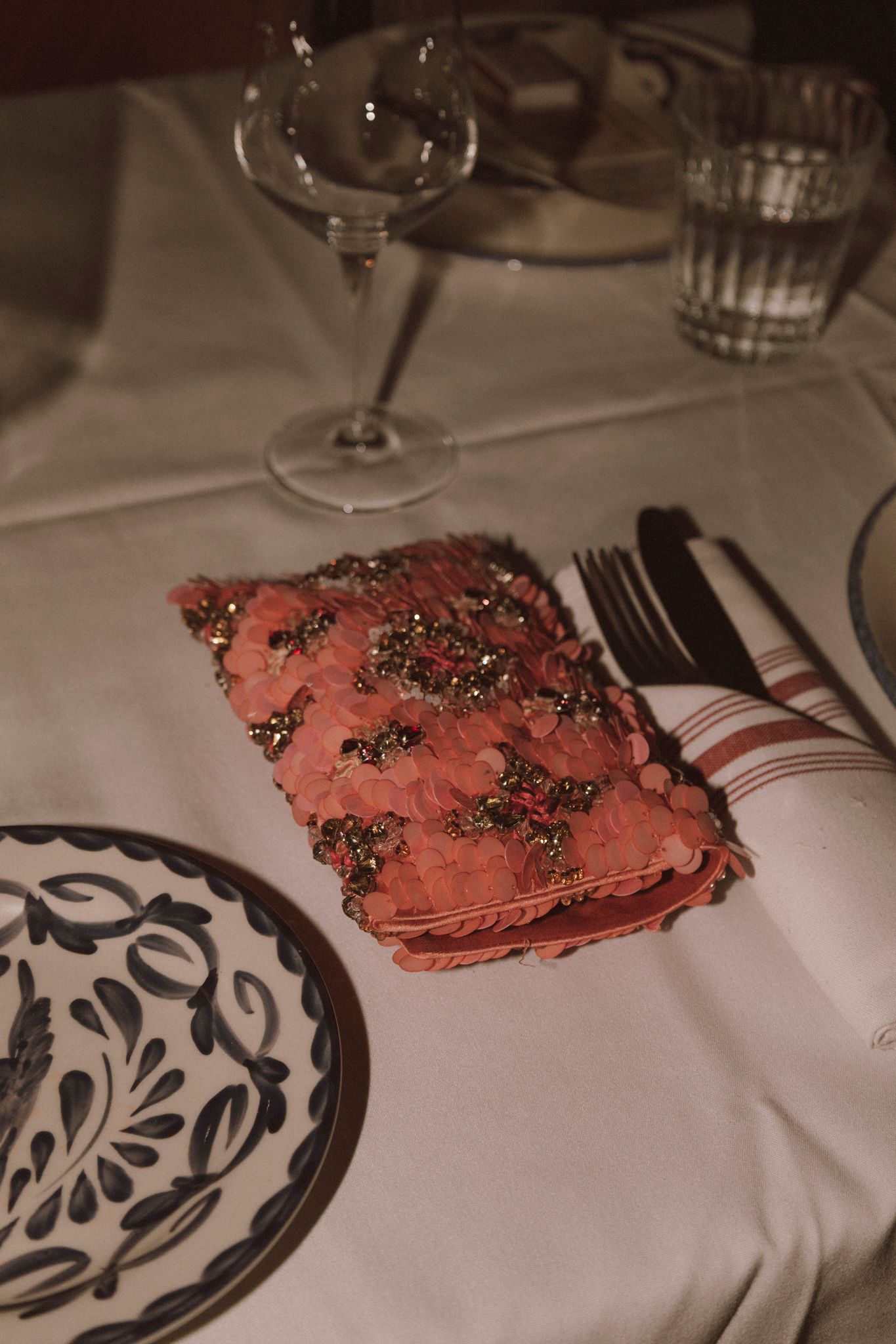 Elegant wedding reception table setting with decorative pink napkin, blue floral plate, silverware, and crystal glassware.