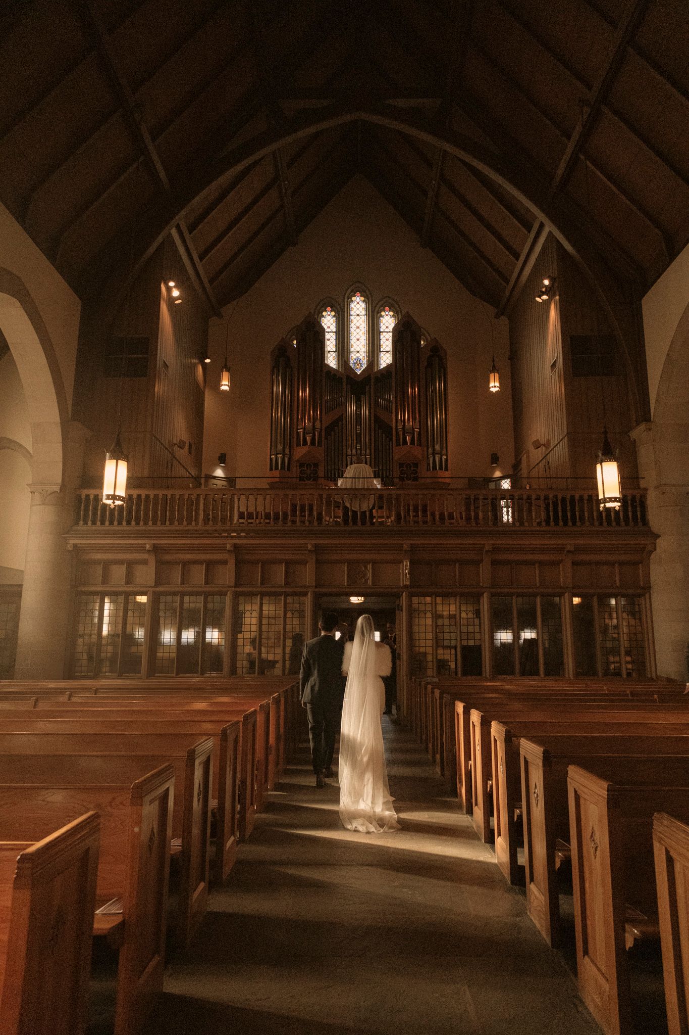 Bride in white veil and groom walk down aisle of grand cathedral church after wedding ceremony.