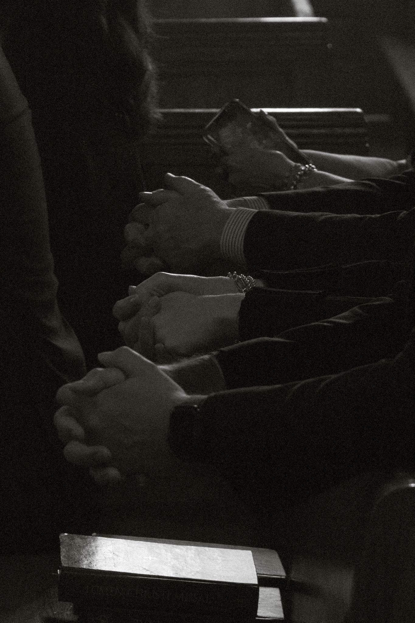Black and white close-up of congregation members with clasped hands in prayer during church service.