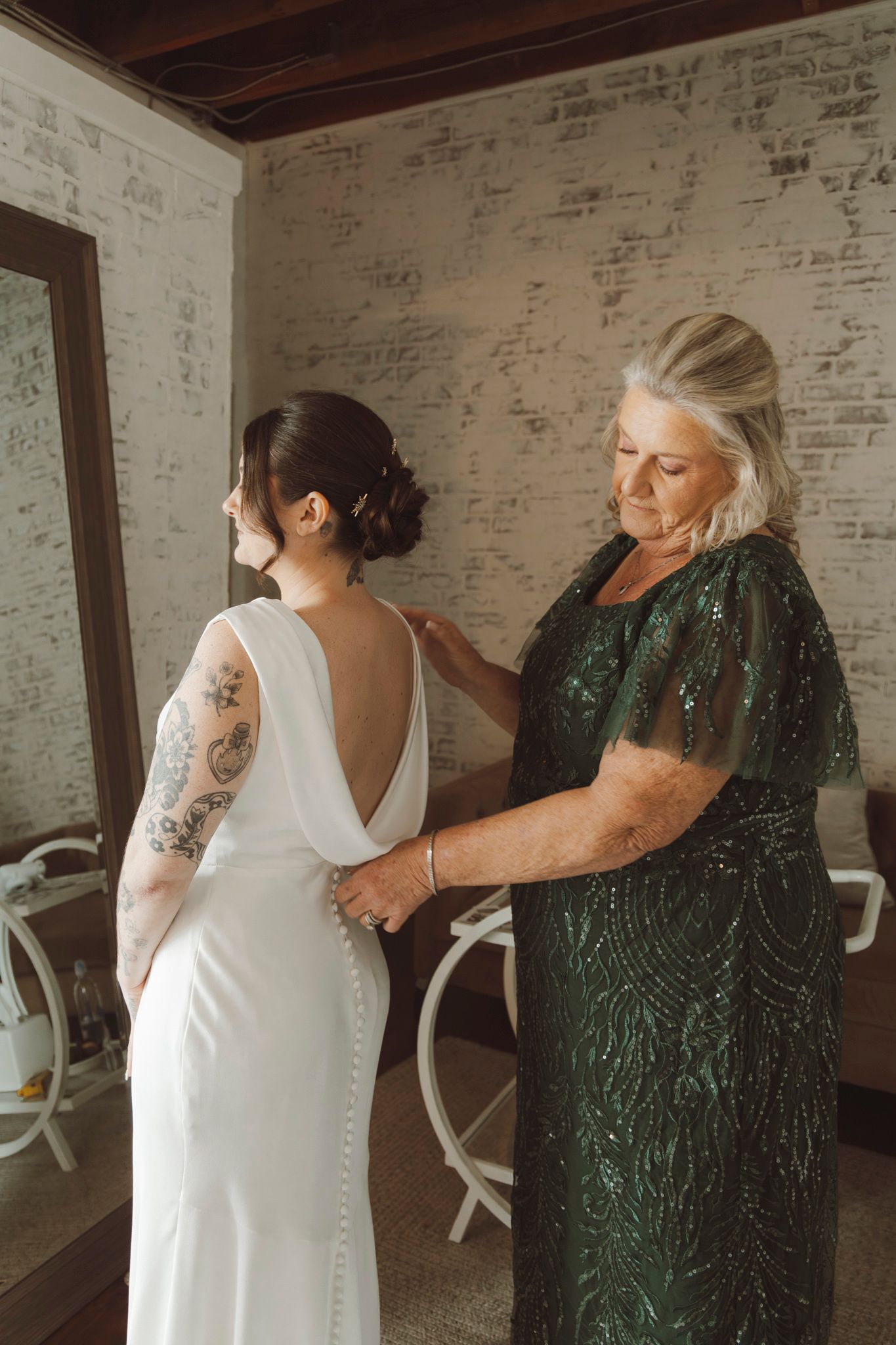 A wedding dress being fitted in a rustic room with exposed brick walls.