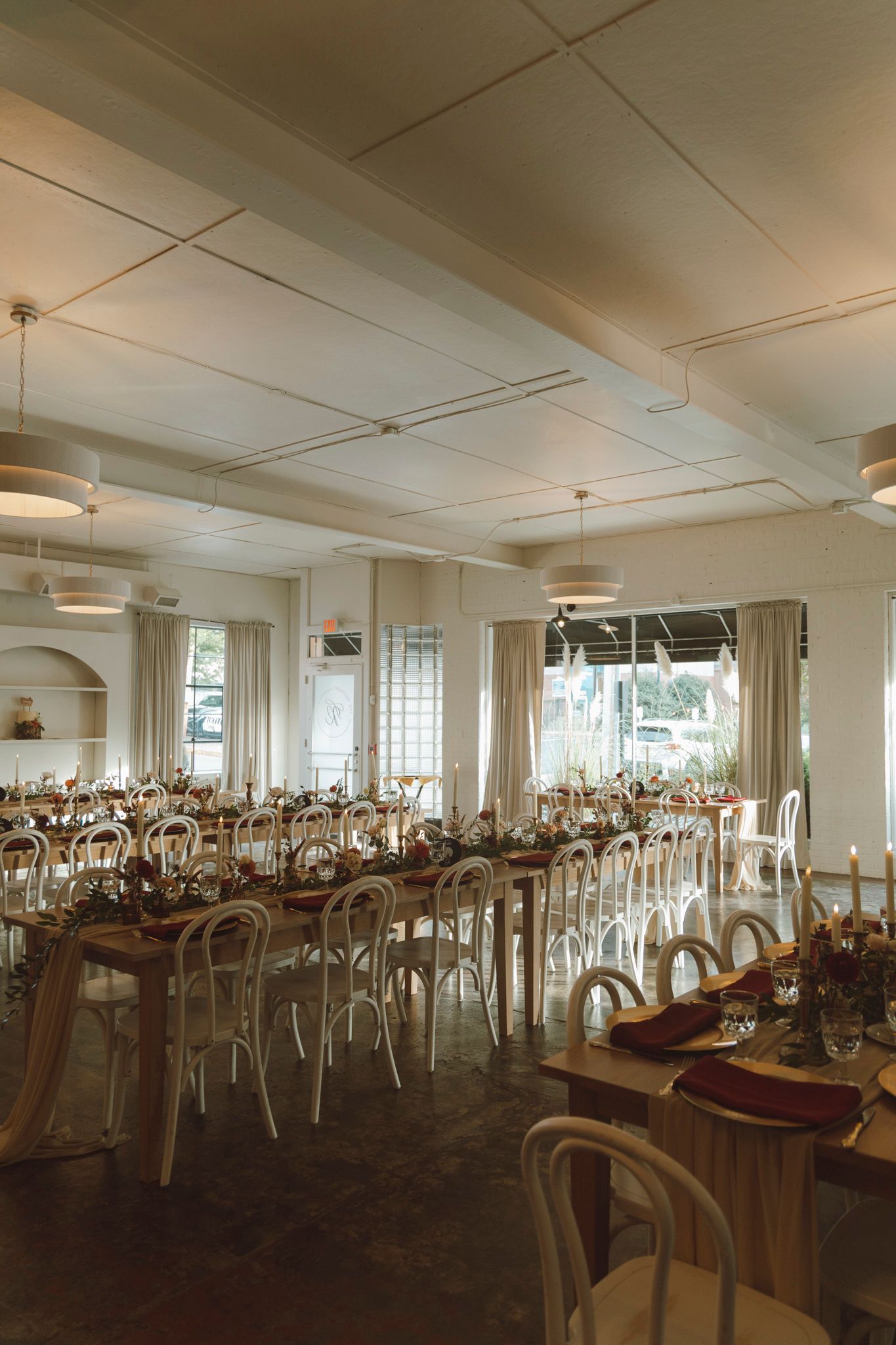 An elegant wedding reception venue with wooden tables, bentwood chairs and romantic lighting in a bright white room.