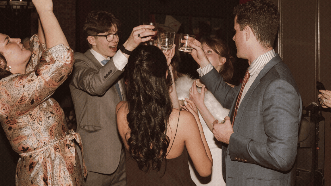 Group of elegantly dressed guests raising glasses in a toast at a festive wedding reception celebration.