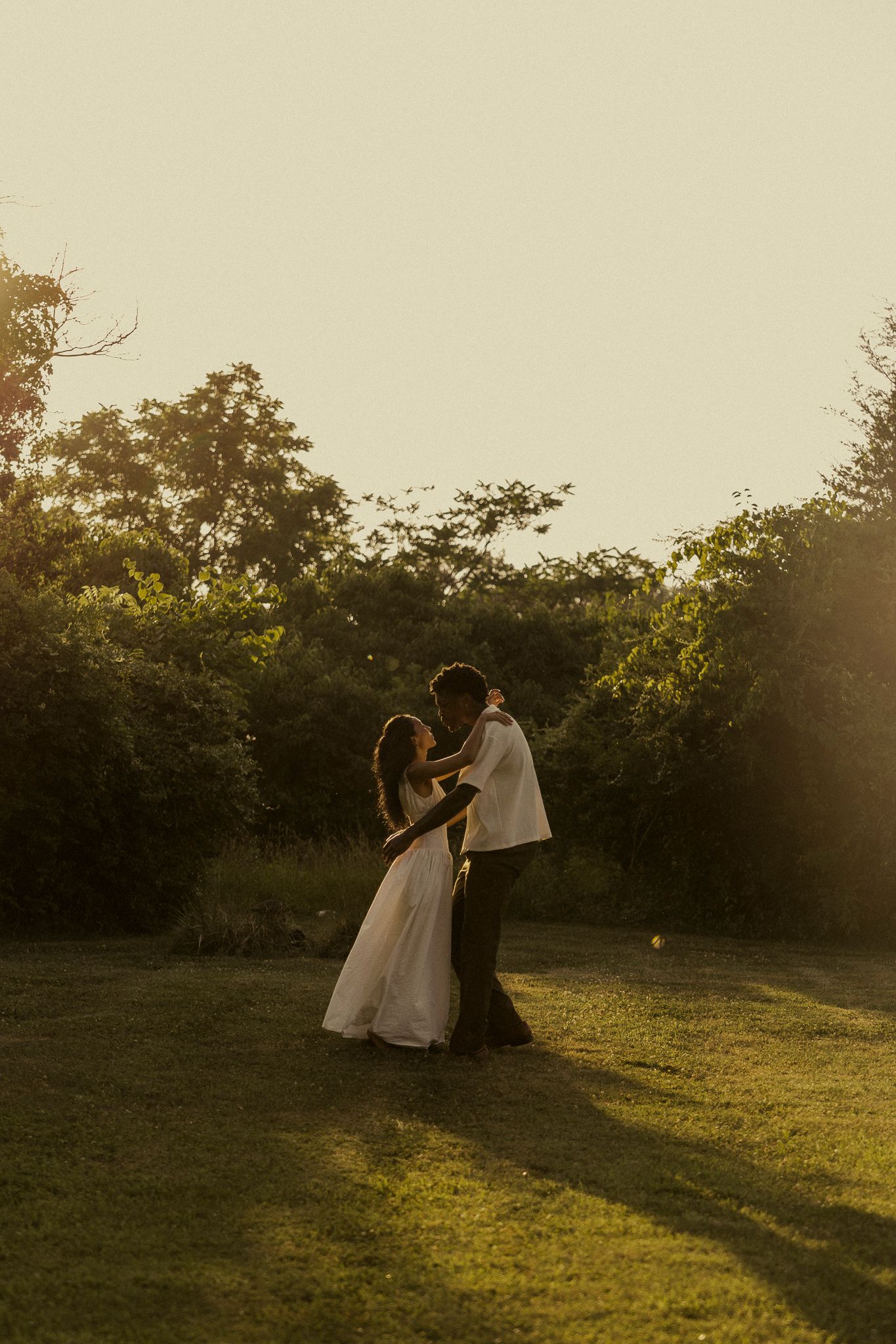 Newlyweds embracing in a sunlit garden at golden hour, bride in white gown and groom in suit.