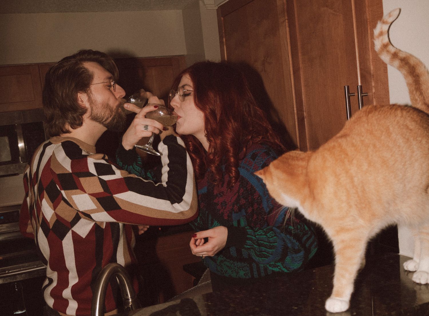 A playful orange cat repeatedly interrupts someone singing into a microphone with affectionate headbutts and nuzzles.