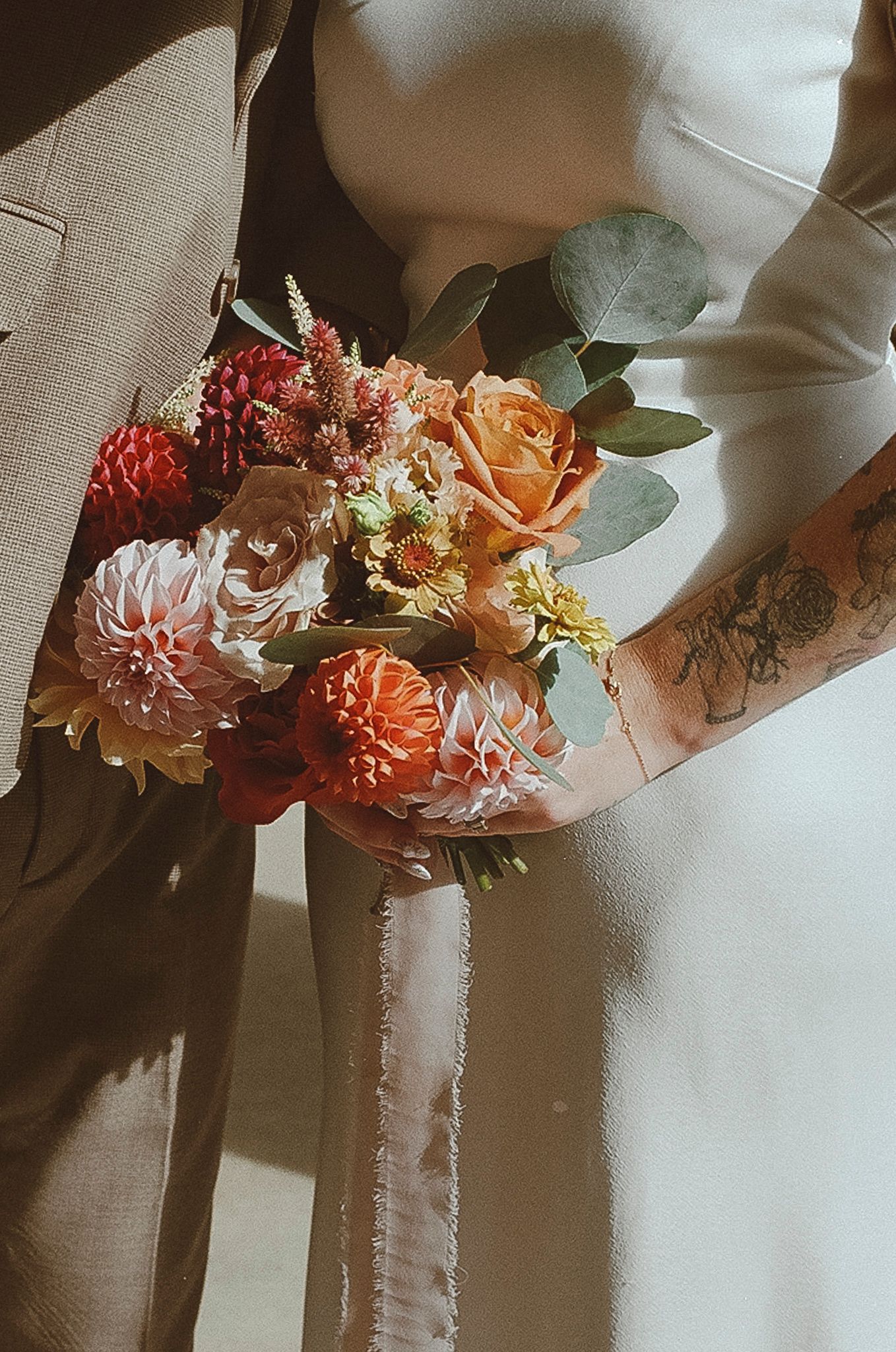 A romantic floral arrangement with peach and coral flowers adorns a white fabric backdrop in soft lighting.
