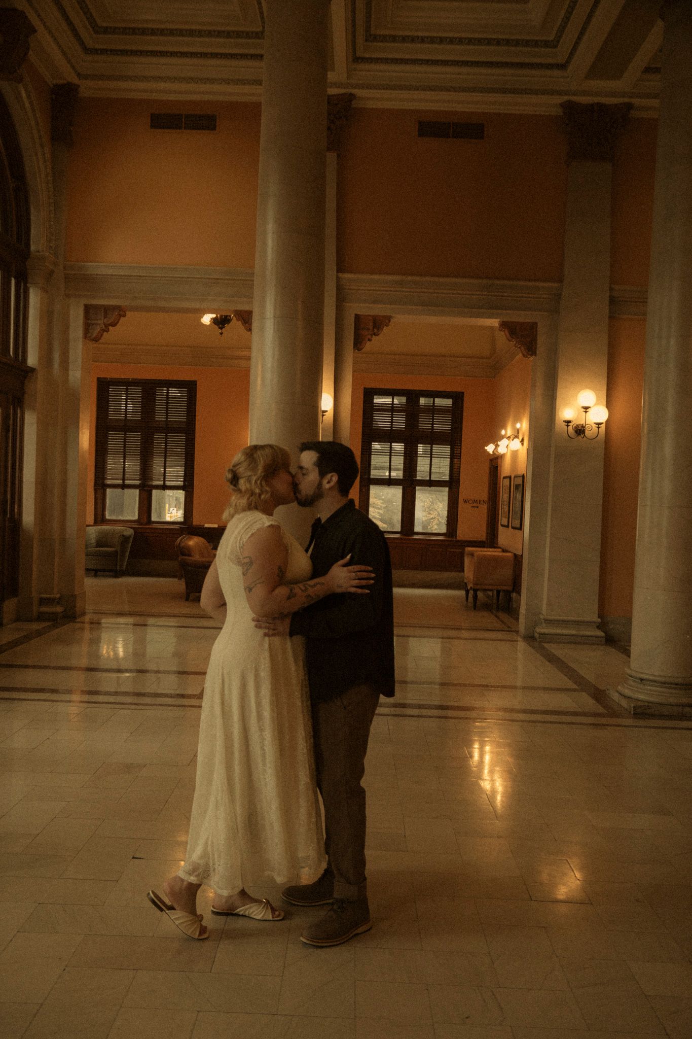 A couple dances together in an elegant ballroom with marble columns and warm lighting creating a romantic atmosphere.