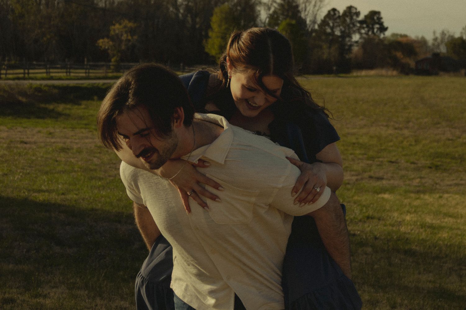 Joyful couple playfully embracing and laughing together in a sunny green field.