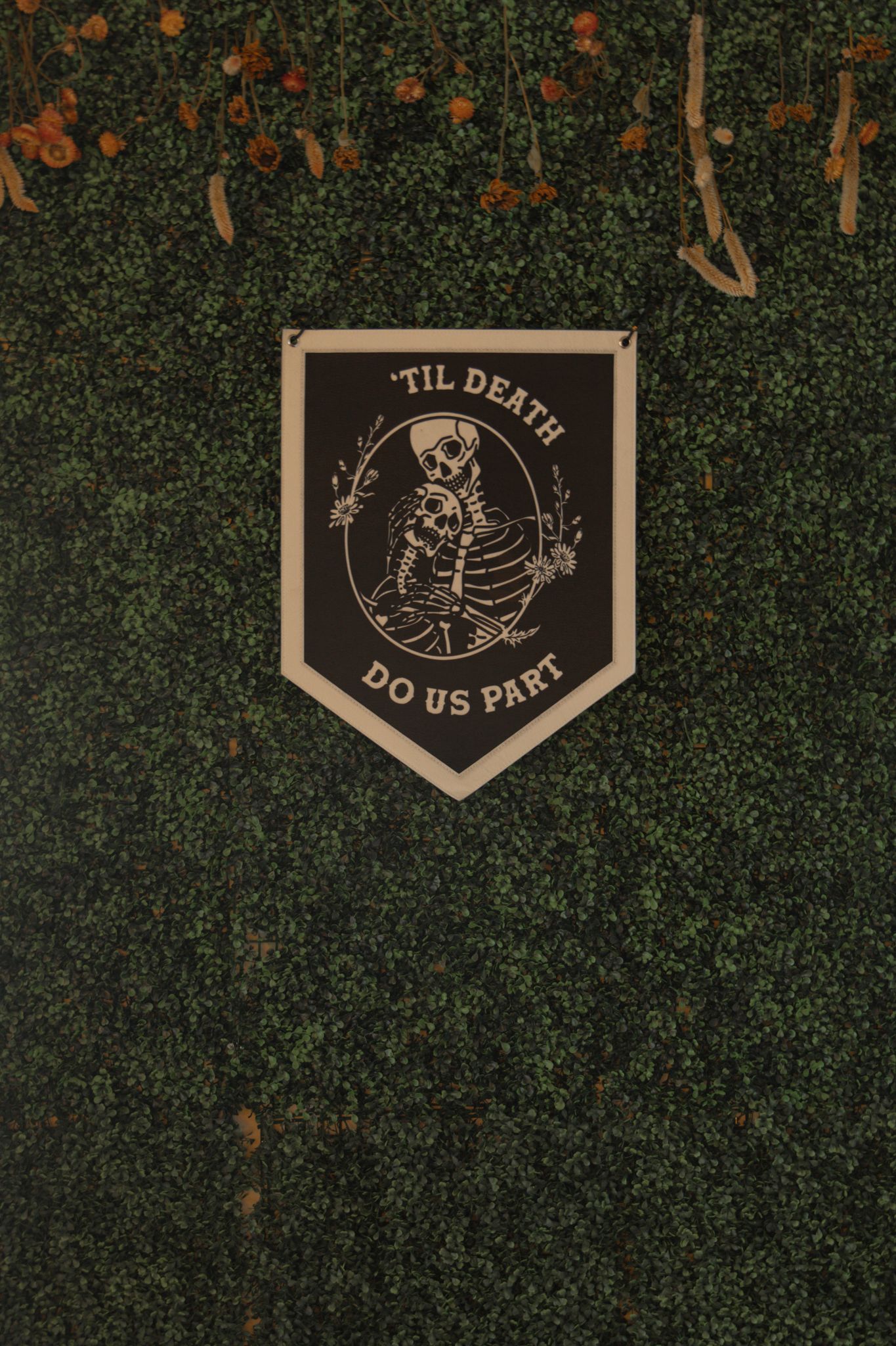 Wedding decor featuring gothic-style banners with skeleton designs and 'Til Death Do Us Part' text against greenery.