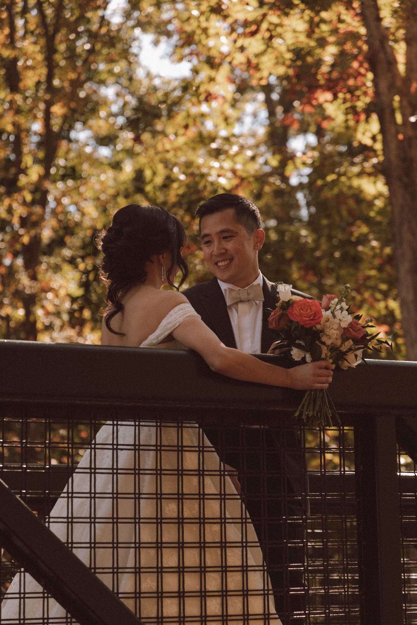 A romantic wedding couple shares an intimate moment on a wooden deck surrounded by autumn foliage.