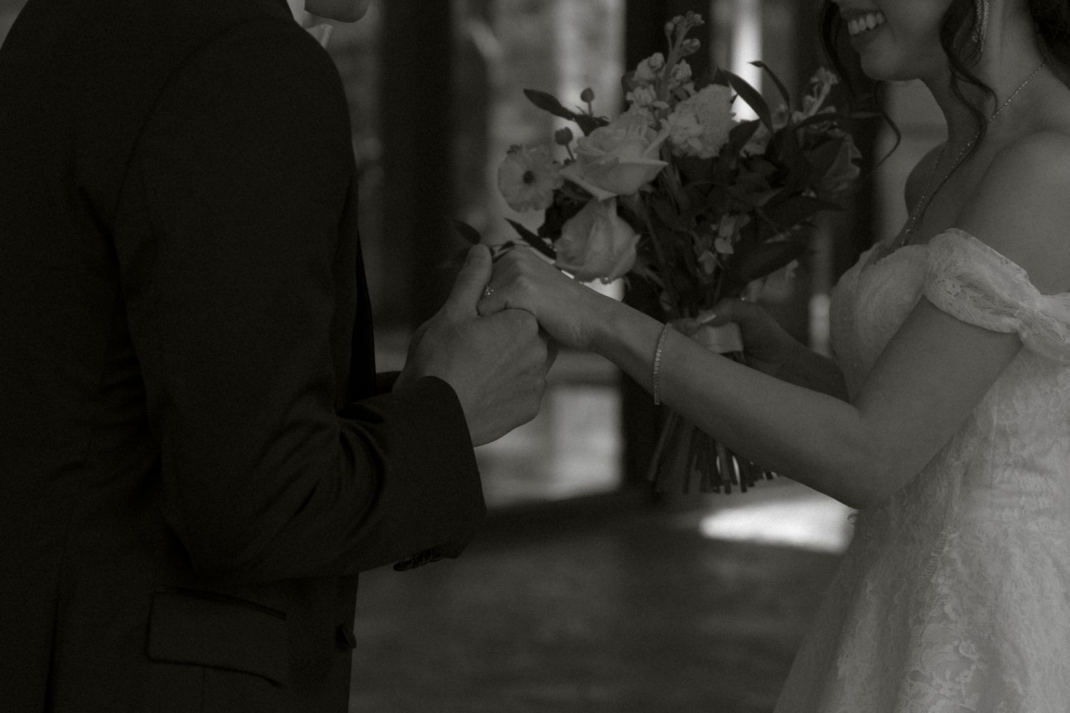 A black and white photo captures a tender moment during a wedding ceremony as hands exchange rings.