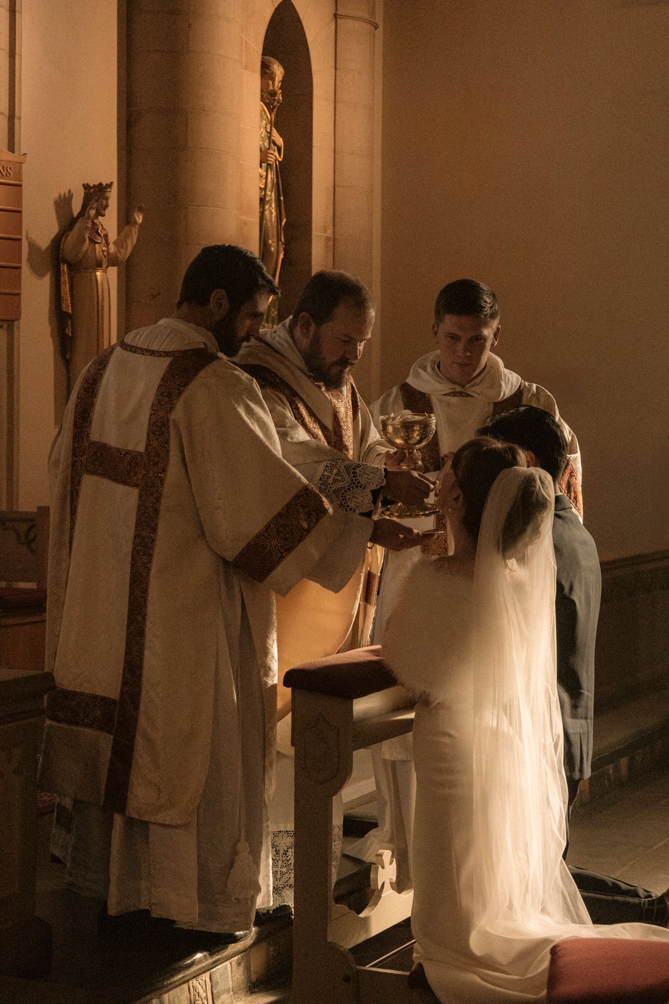 Priest offering communion chalice to kneeling bride at church altar during wedding mass.