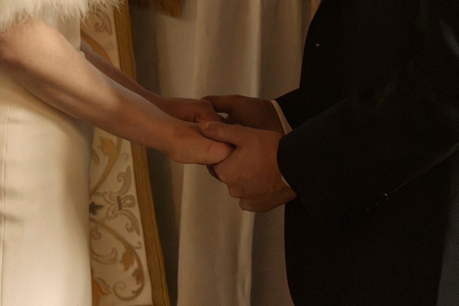 Bride and groom holding hands during wedding ceremony, close-up of interracial couple joining hands.