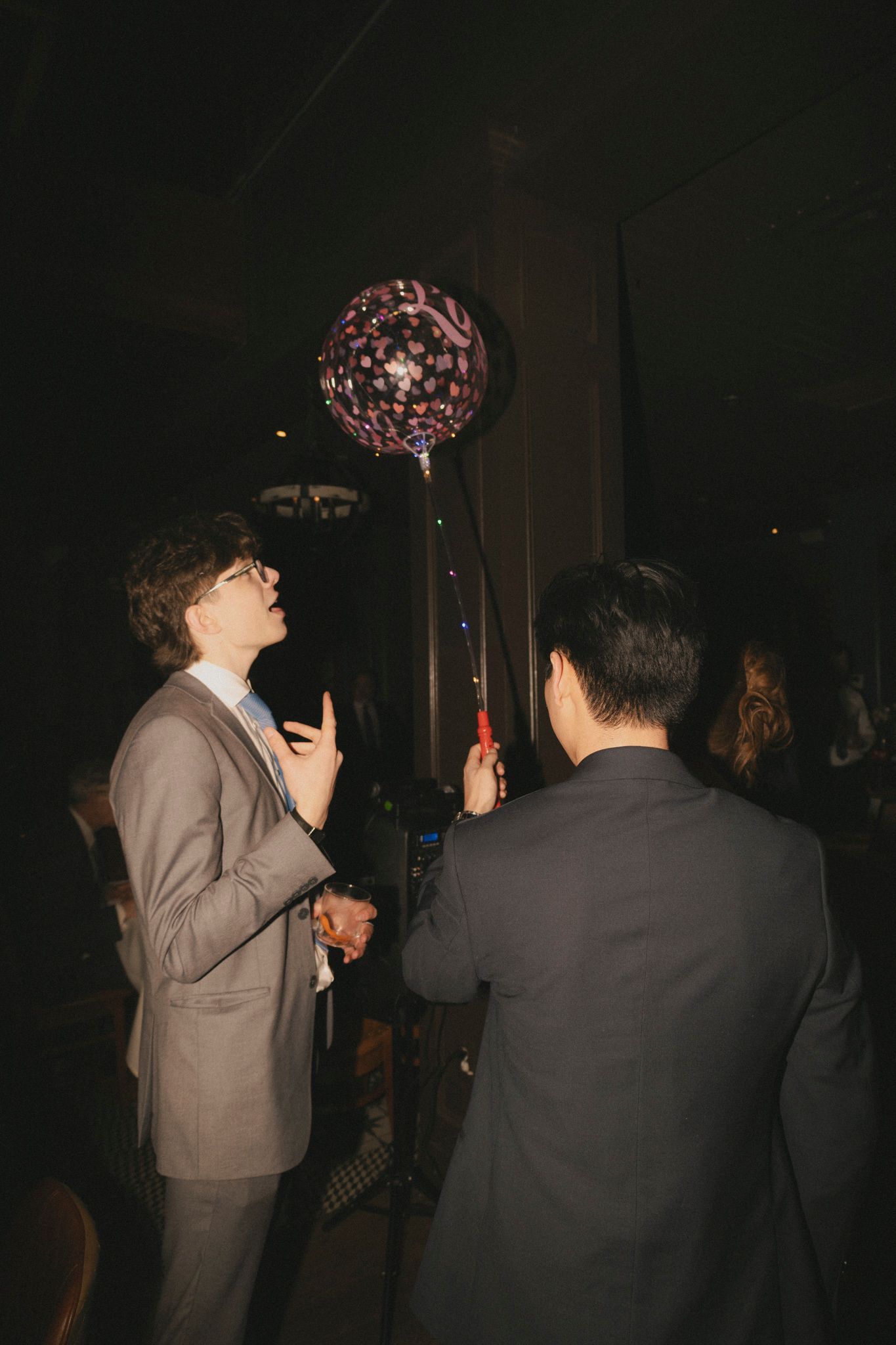 Two men in suits admire a large decorative balloon at an elegant wedding reception venue.