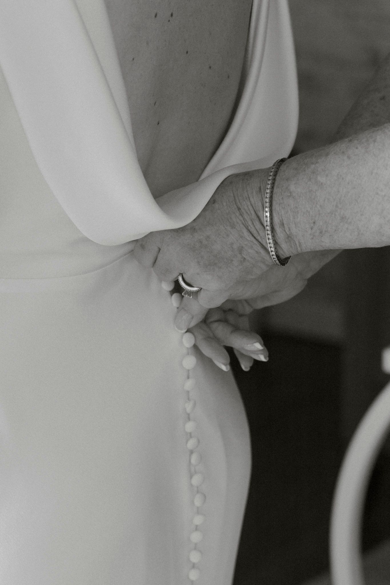 Close-up black and white photo of delicate button details on the back of a white wedding dress.