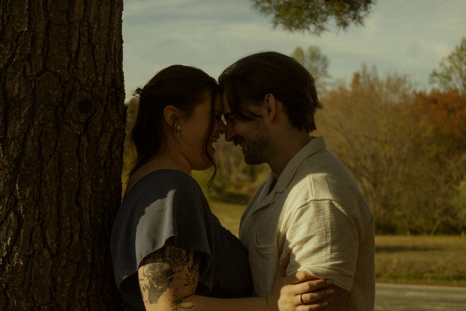 Romantic couple sharing an intimate moment near a tree in a scenic outdoor park setting.