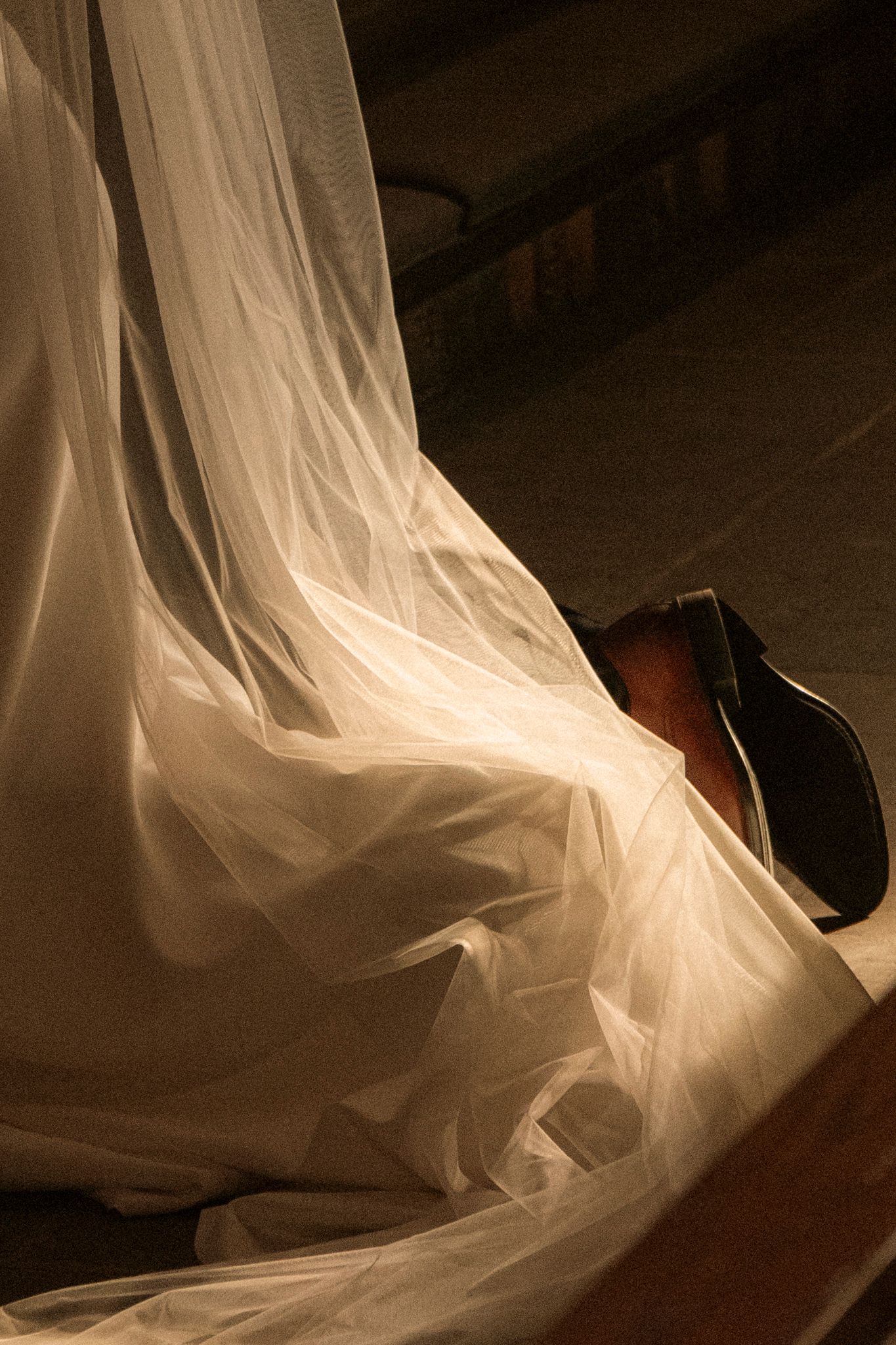 Close-up of brides flowing white veil and train pooling on church floor beside wooden pew.