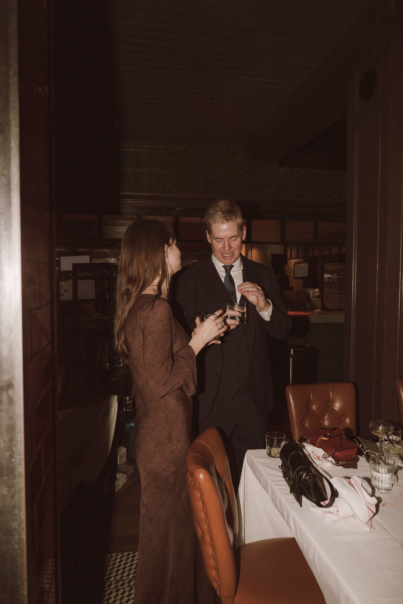 Couple shares an intimate moment near a white-draped table at a dimly lit wedding reception.