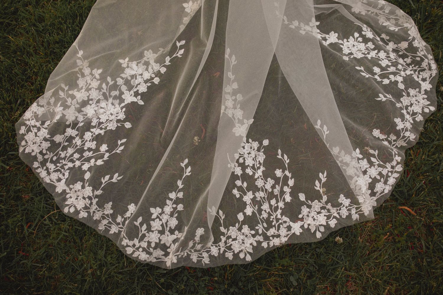 A white wedding dress train with delicate lace details spreads out on green grass creating an elegant bridal photo.