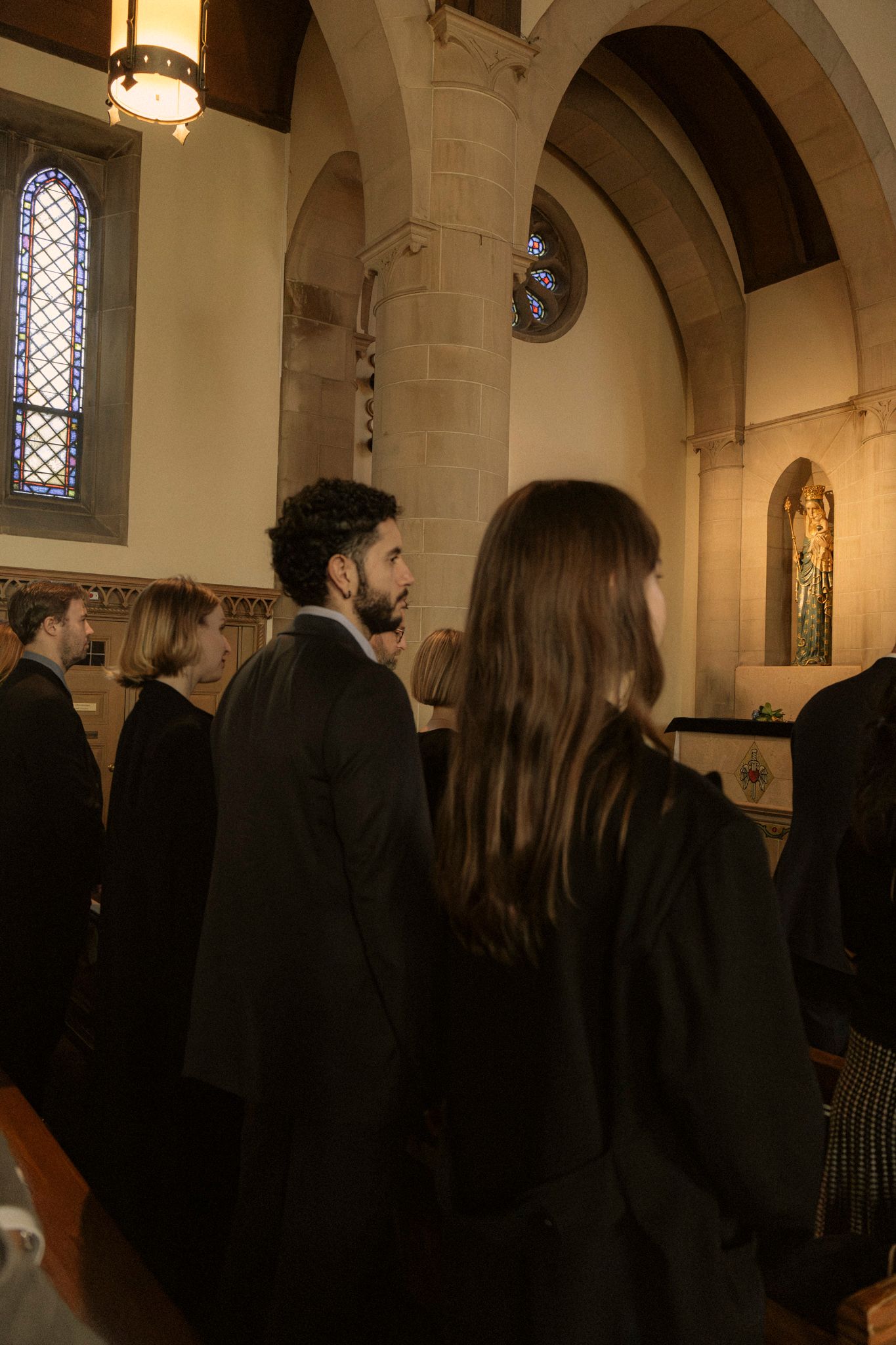 Wedding guests dressed in black attire standing inside a historic stone church during a ceremony.