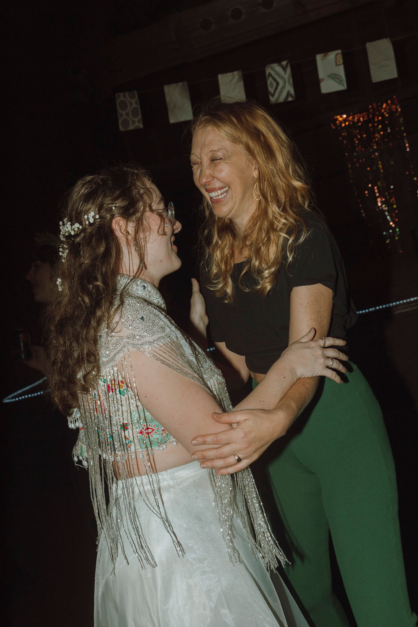 Two people share a joyful moment dancing together at a party, one wearing a sparkly dress and one in green pants.