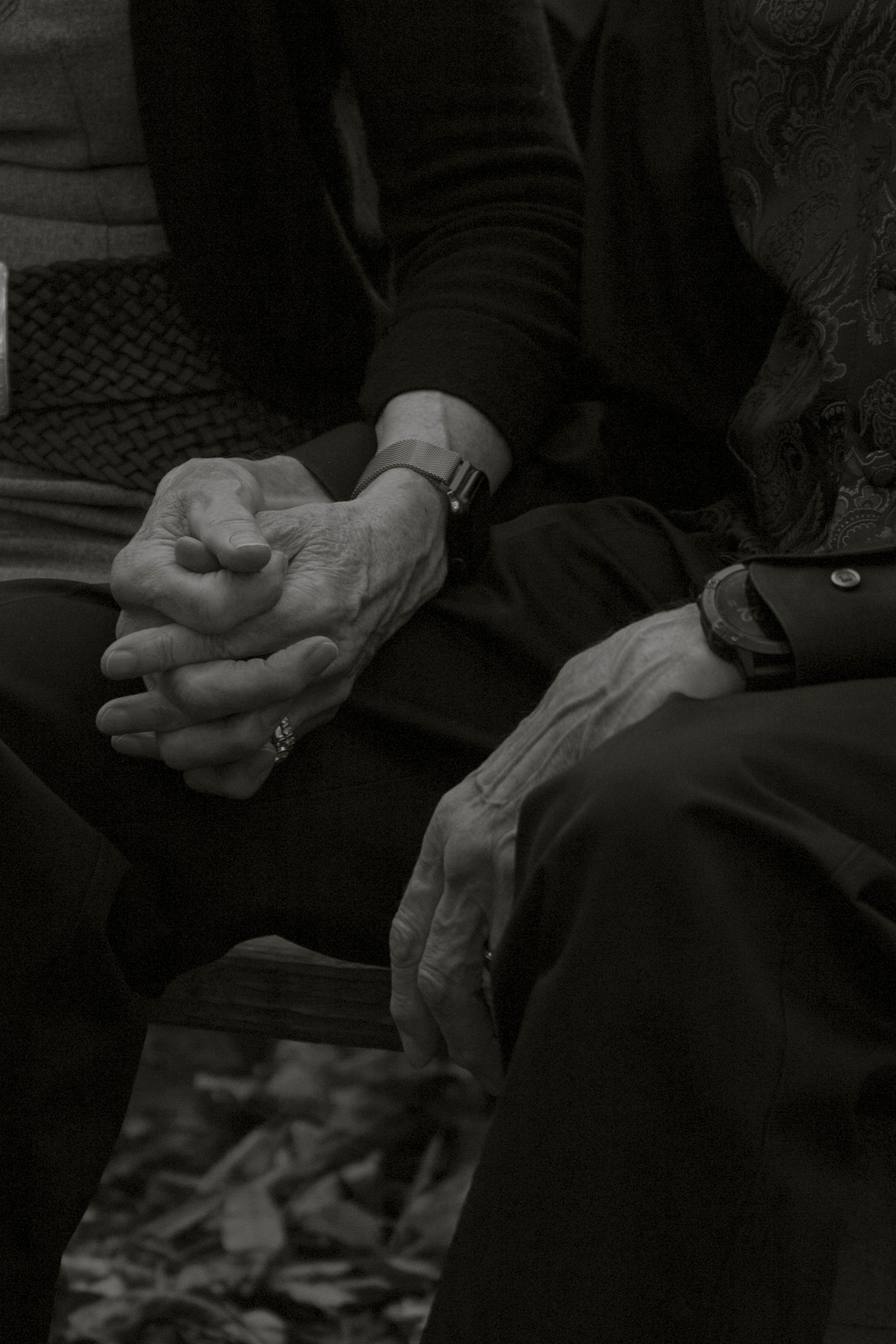 A black and white close-up photograph of elderly hands clasped together while sitting.